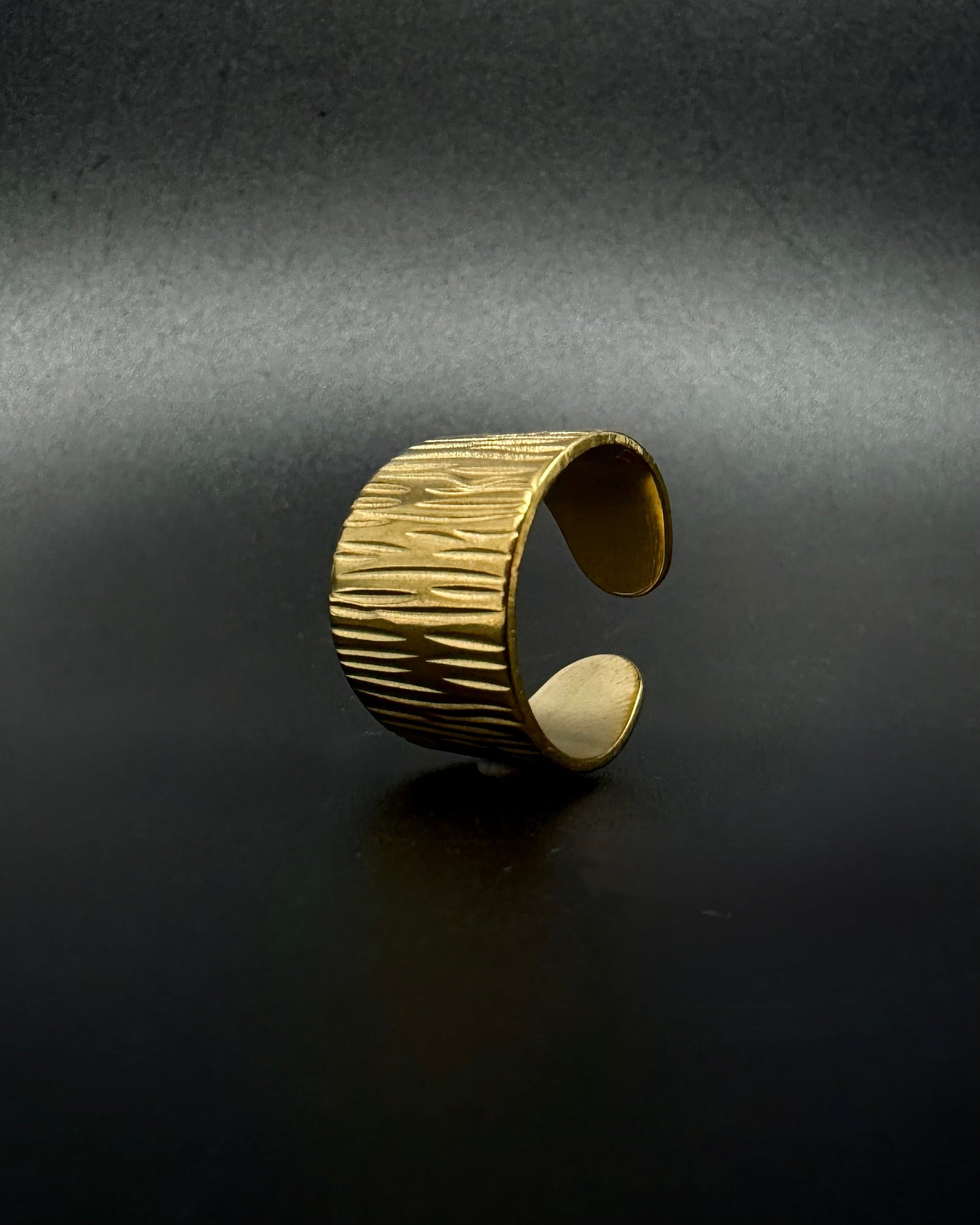 Gold Theia Frequency adjustable ring with a wide tapered band and irregular linear waveform texture against a black background.