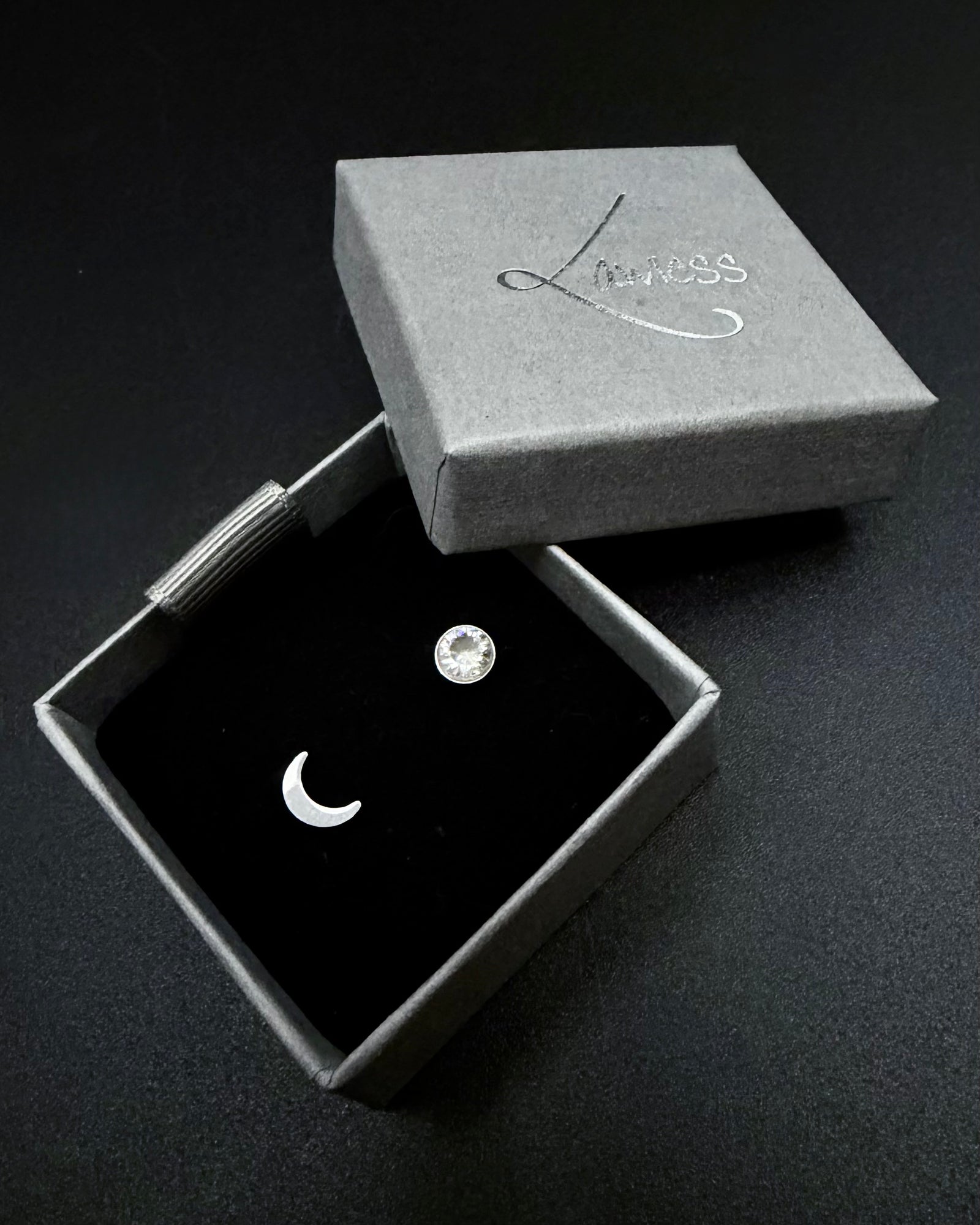 Jewelry box with a crescent moon earring and round gemstone on a dark background