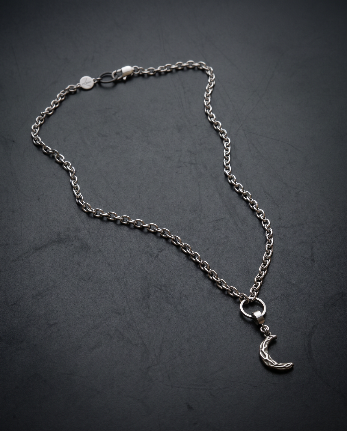 Silver Hecate Keeper Charm on Necklace with a sculptural crescent shape, raised organic markings and a wide stainless steel bail against a black background.