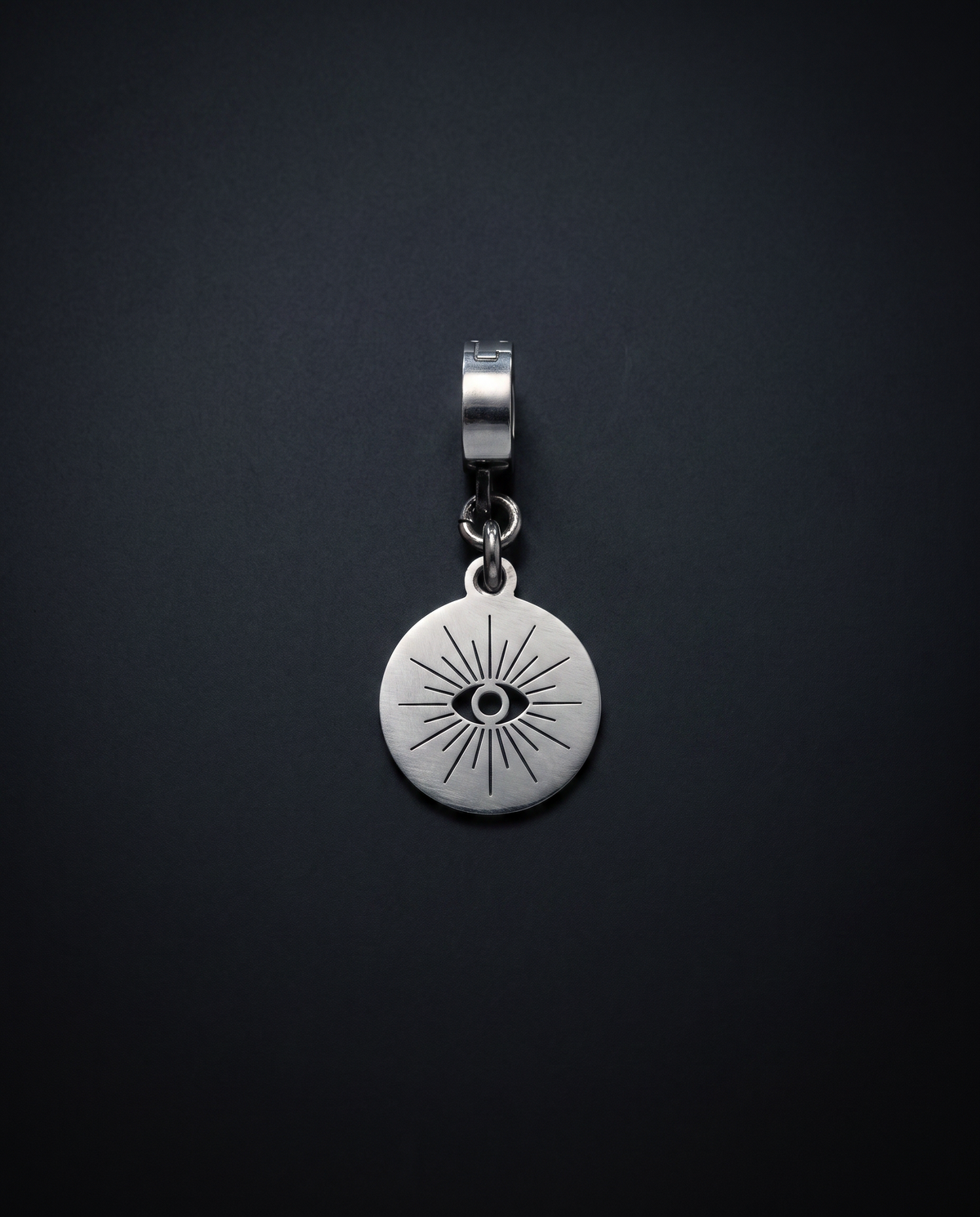 Round silver Hecate Oracle Charm with a central cut-out eye and radiating line design against a black background.