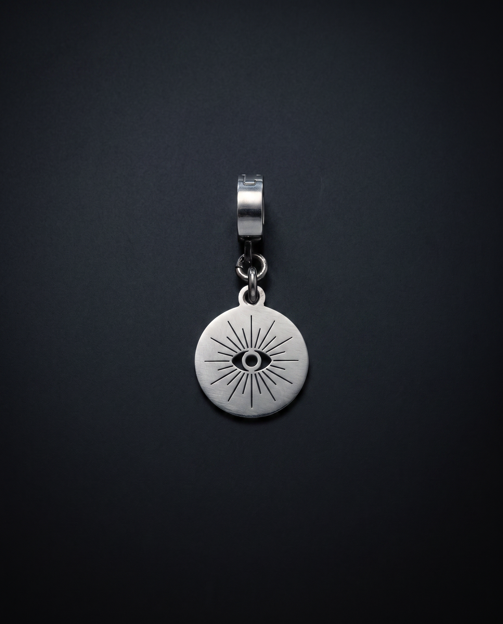 Round silver Hecate Oracle Charm with a central cut-out eye and radiating line design against a black background.