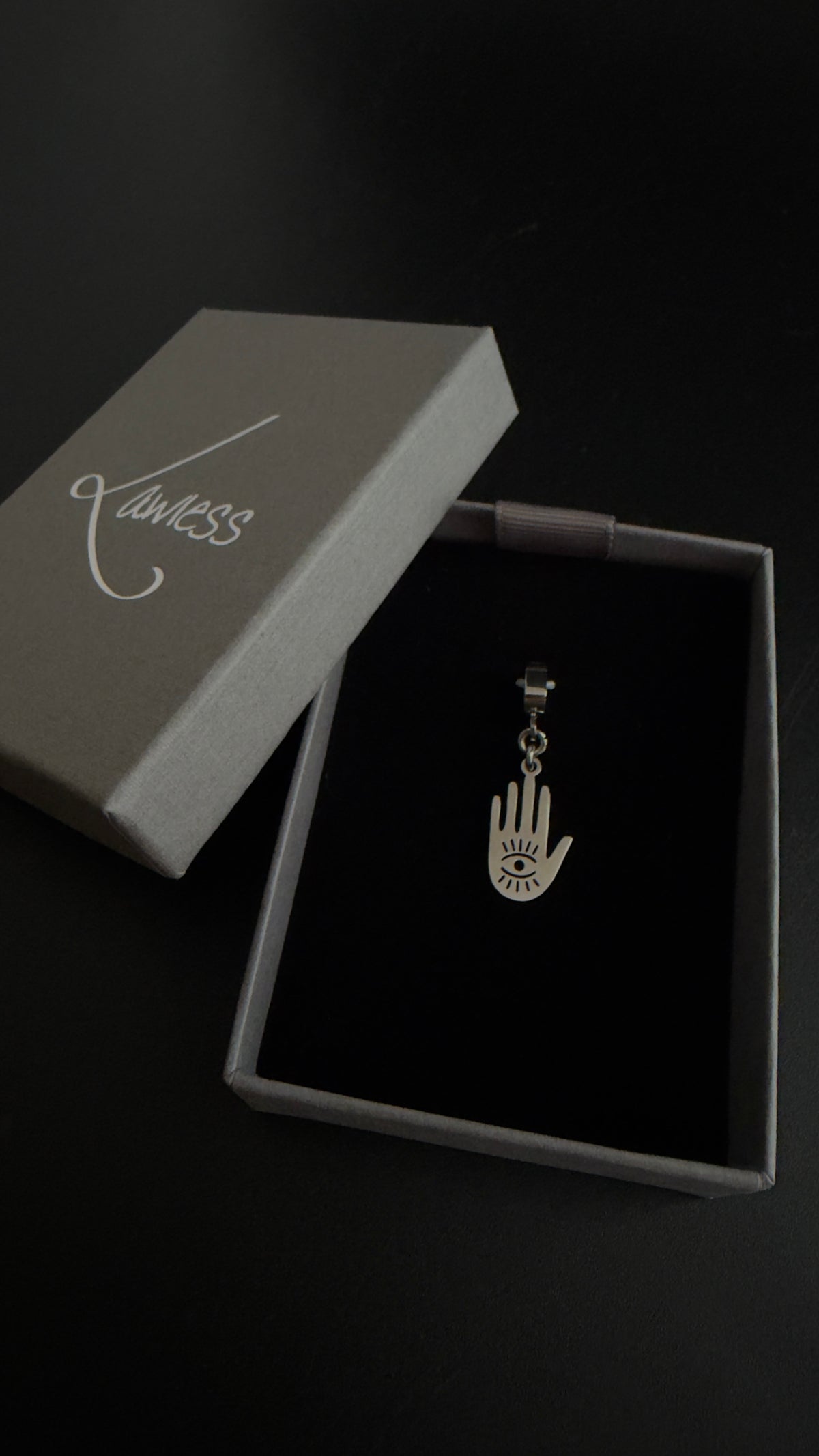 Silver Hecate Protector Charm shaped as an open hand with a watchful eye and radiating cut-out details, displayed against a black background.