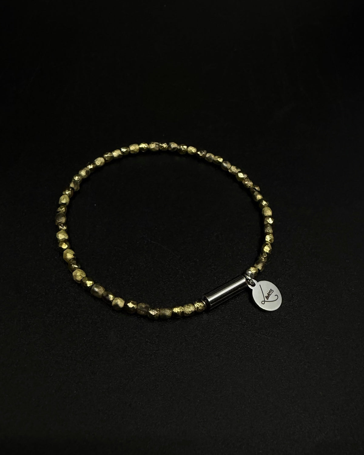 Gold Eos Flare Bracelet made from faceted burnished-gold crystal beads with a silver screw clasp and round Lawless logo tag against black background.