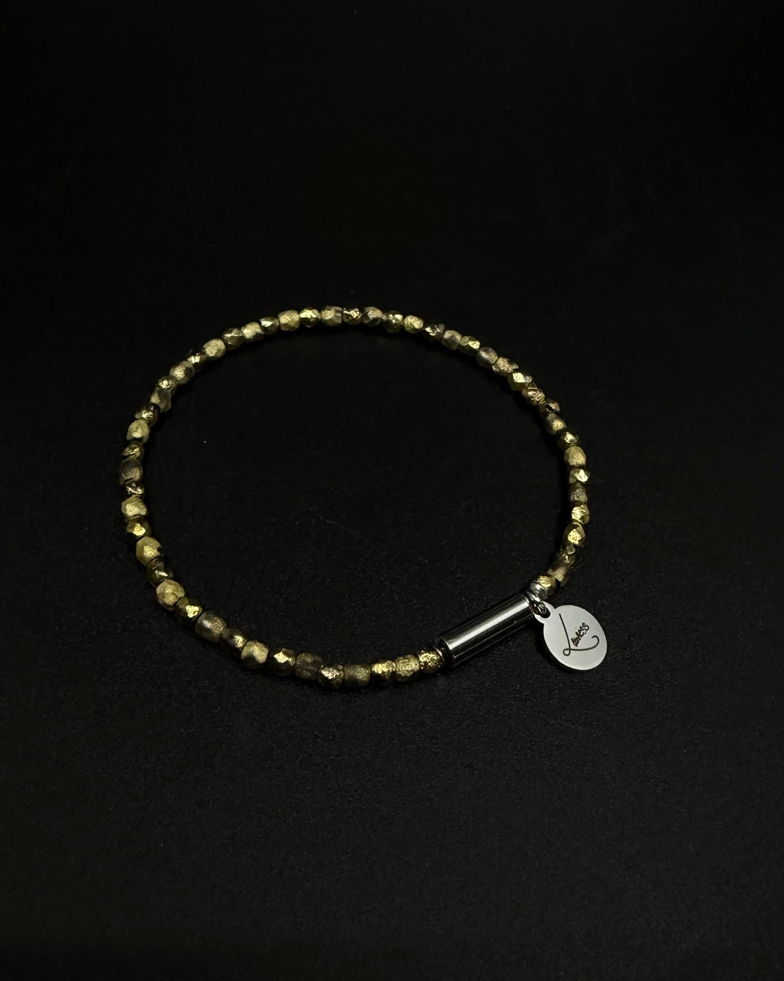 Gold Eos Flare Bracelet made from faceted burnished-gold crystal beads with a silver screw clasp and round Lawless logo tag against black background.