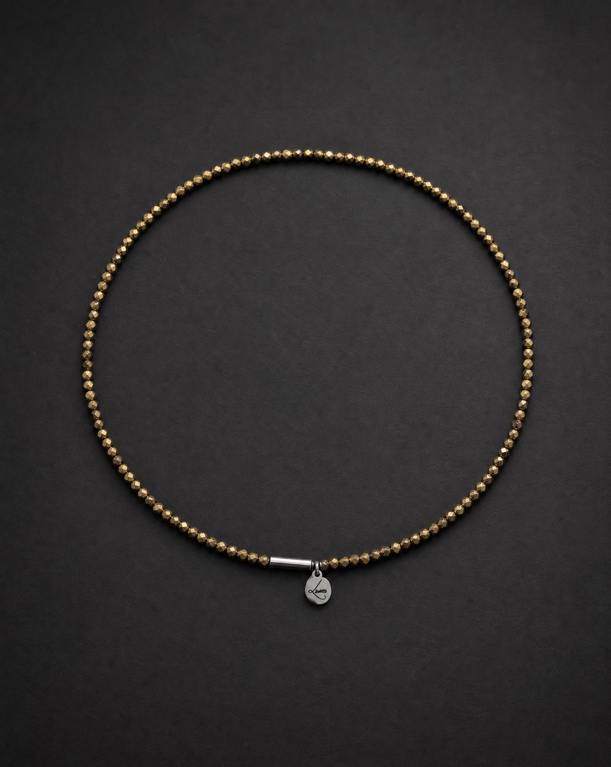 Eos Flare Necklet arranged against a black background, featuring faceted metallic gold crystal beads, a silver screw clasp and silver Lawless logo tag.
