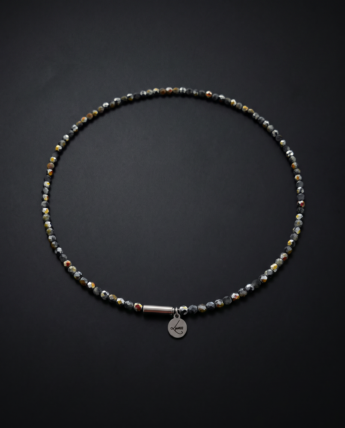 Dark Eos Flare beaded necklet arranged against a black background, featuring faceted crystal beads with metallic flashes and a stainless steel screw clasp.