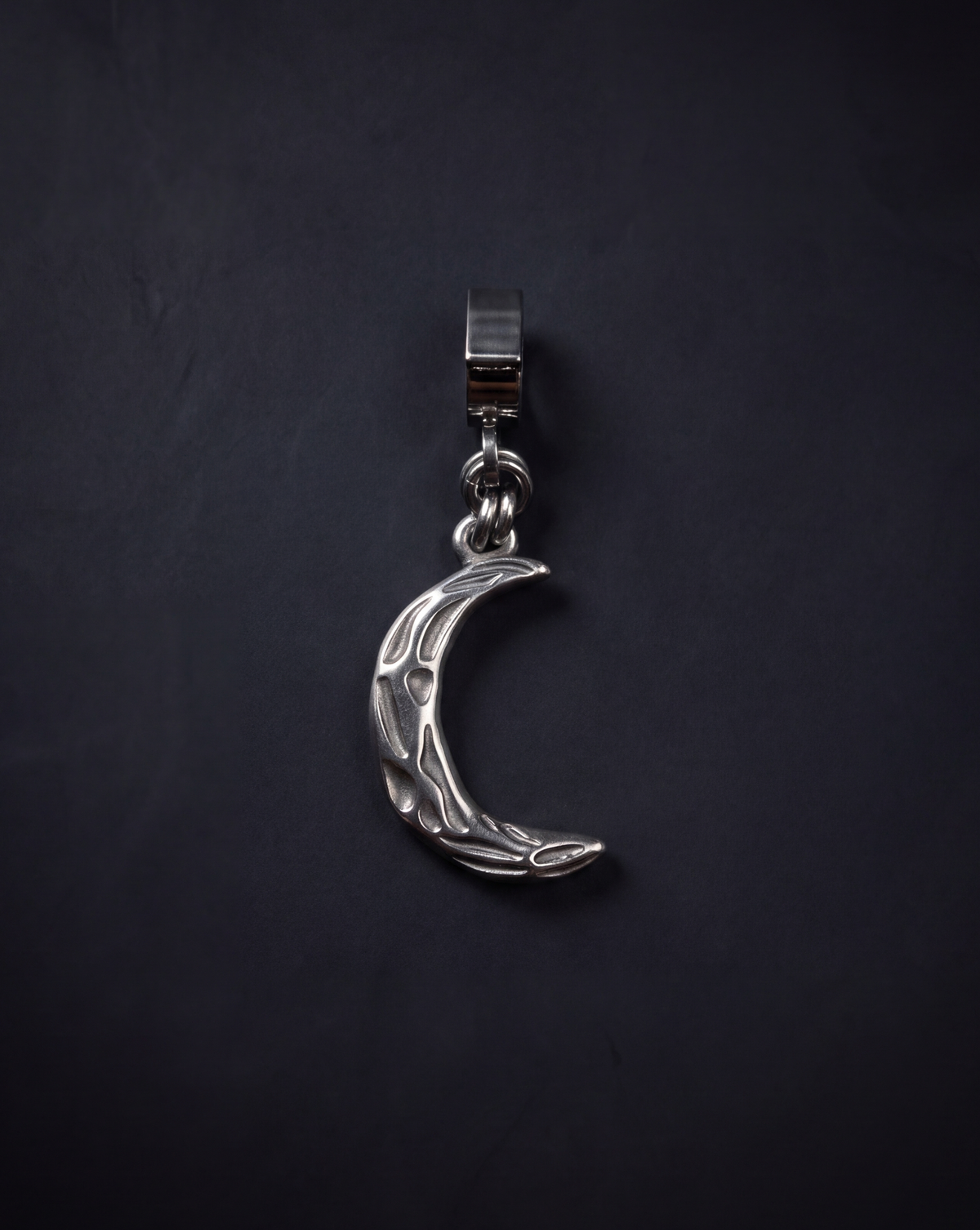 Silver Hecate Keeper Charm with a sculptural crescent-moon shape, raised organic markings and a wide stainless steel bail against a black background.