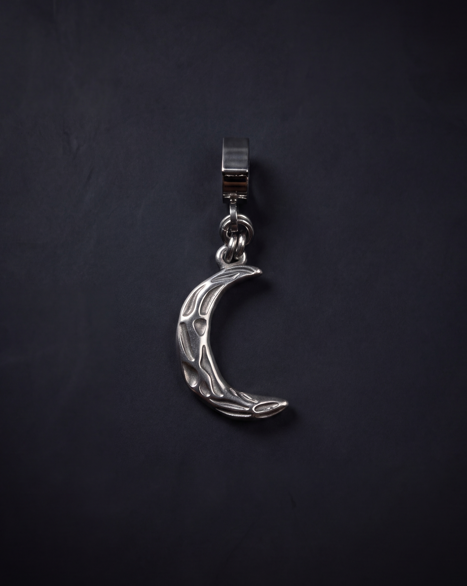 Silver Hecate Keeper Charm with a sculptural crescent-moon shape, raised organic markings and a wide stainless steel bail against a black background.