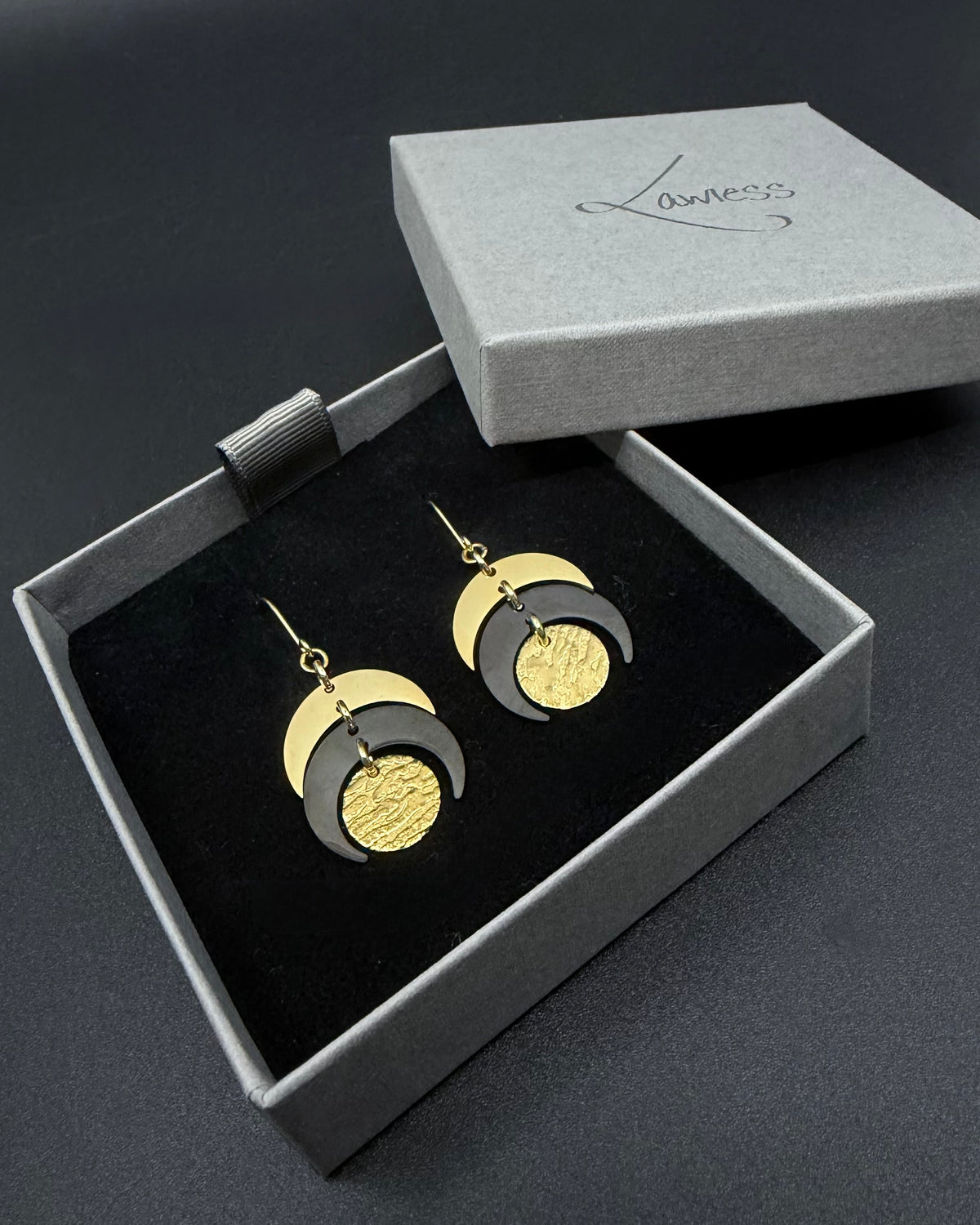 Pair of Luna Phase drop earrings with polished gold crescent forms and a textured black central disc suspended from hook ear wires.