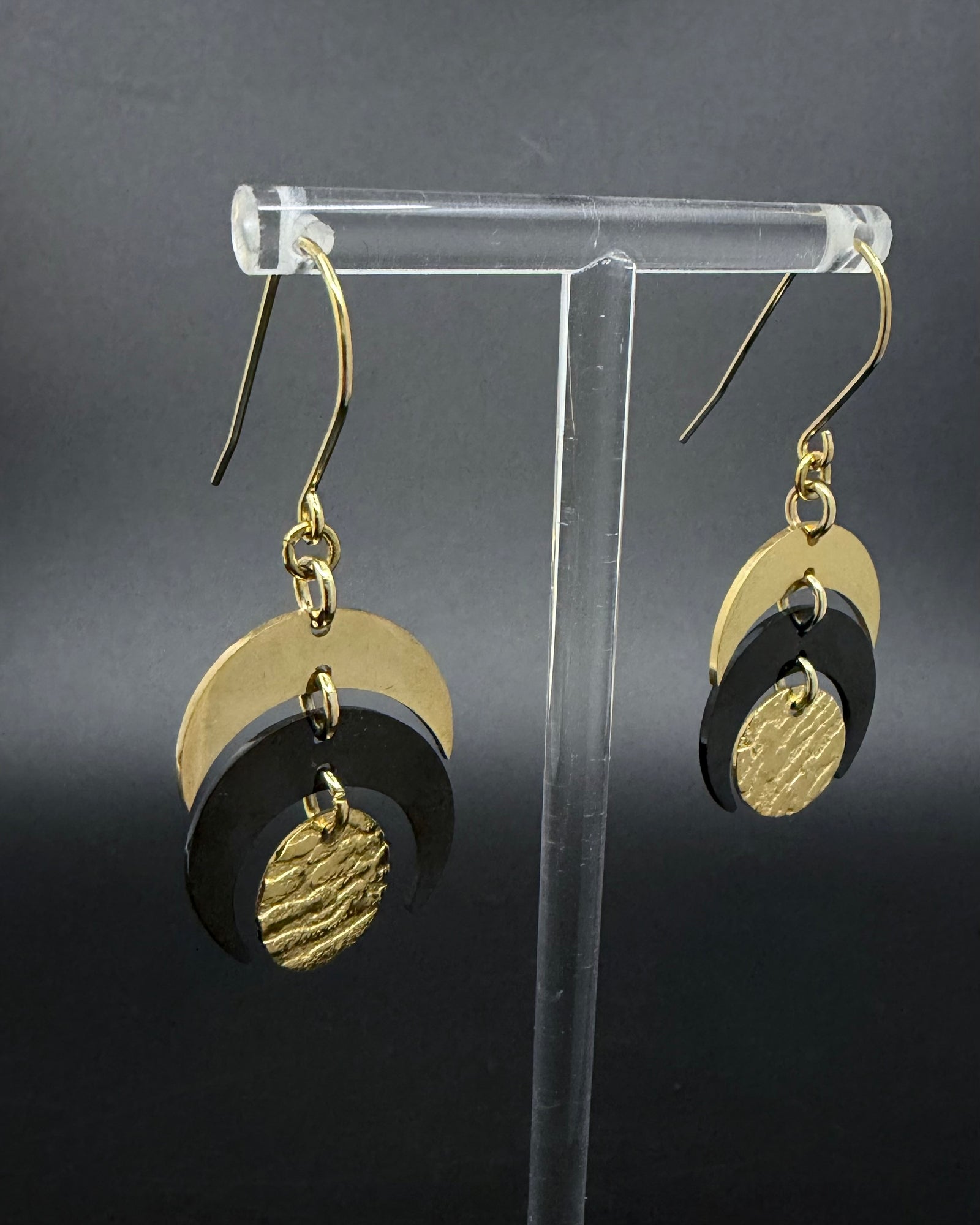 Pair of Luna Phase drop earrings with polished gold crescent forms and a textured black central disc suspended from hook ear wires.