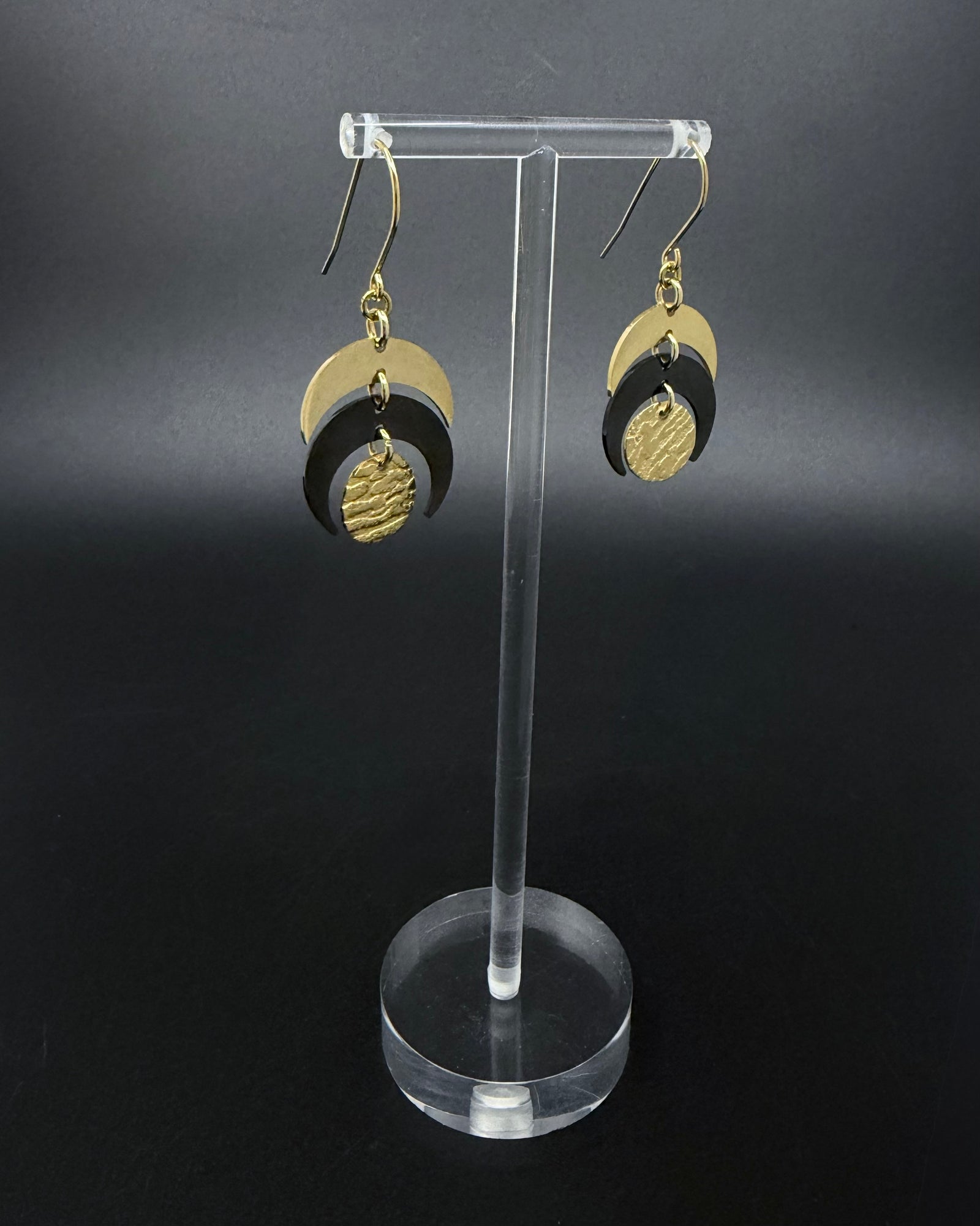 Pair of Luna Phase drop earrings with polished gold crescent forms and a textured black central disc suspended from hook ear wires.