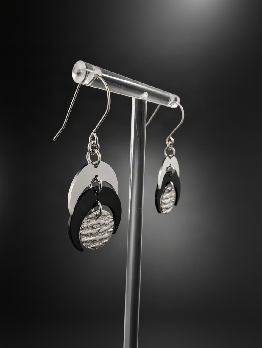 Pair of Luna Phase drop earrings with polished silver crescent forms and a textured black central disc suspended from silver hook ear wires.