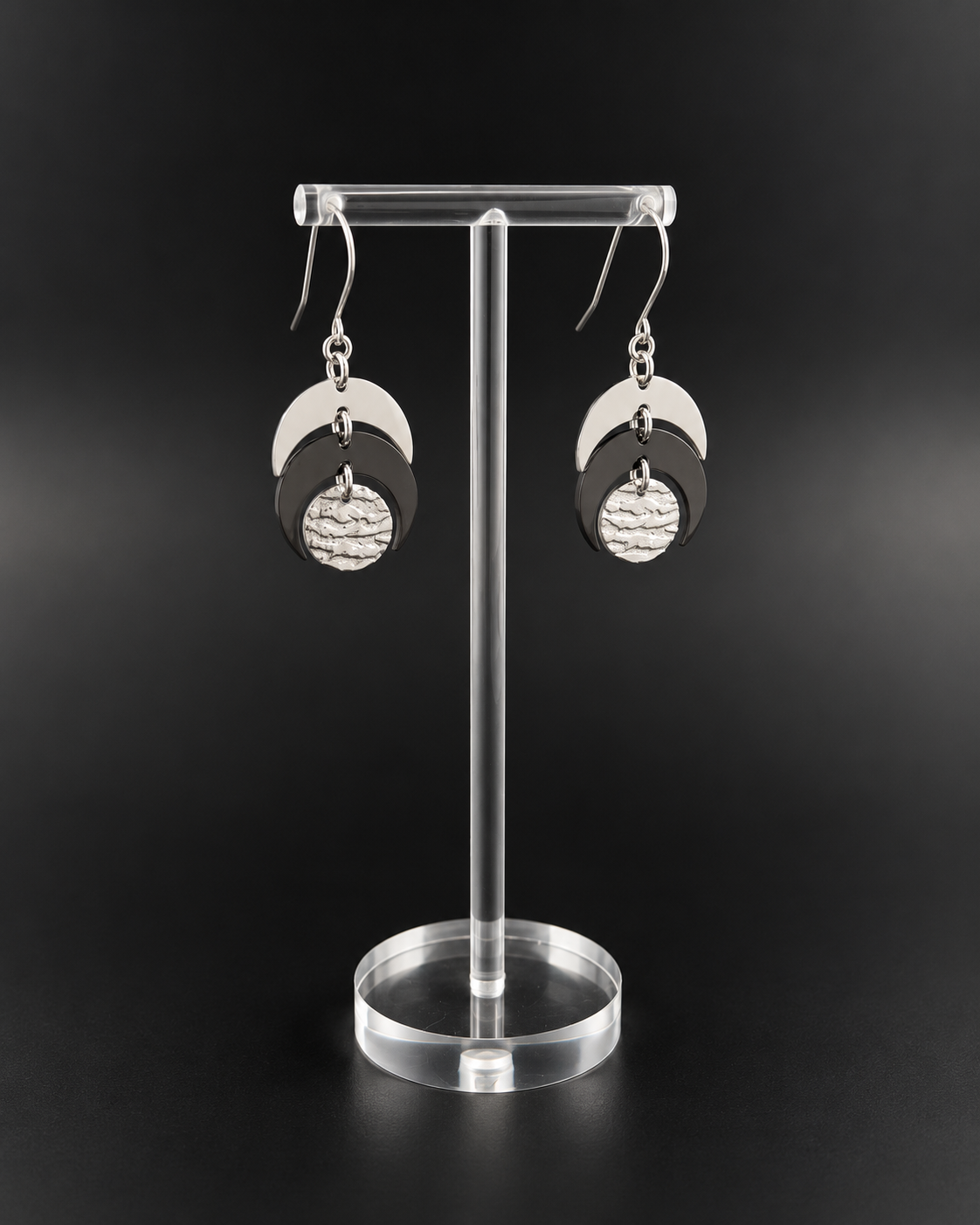 Pair of Luna Phase drop earrings with polished silver crescent forms and a textured black central disc suspended from silver hook ear wires.
