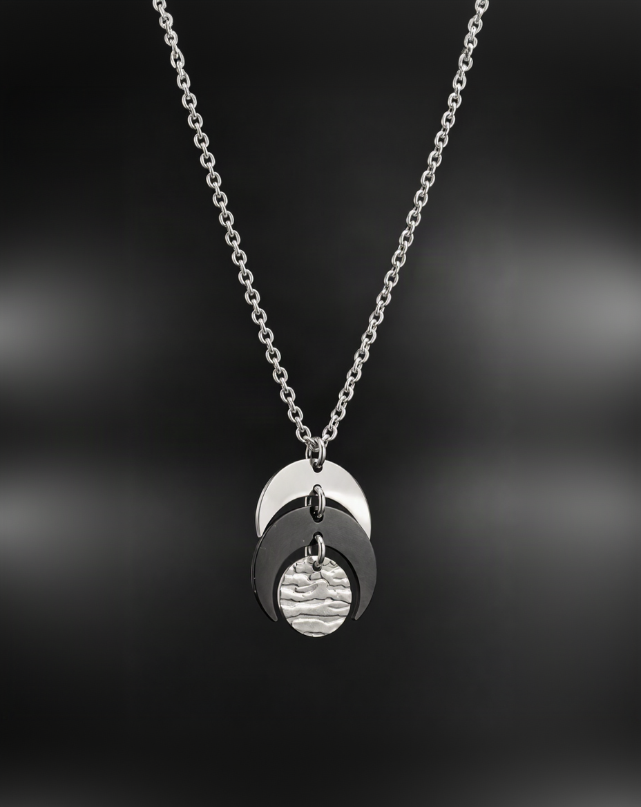 Silver and black Luna Phase Necklace featuring layered crescent shapes and a textured silver lunar disc on a silver chain against a black background.