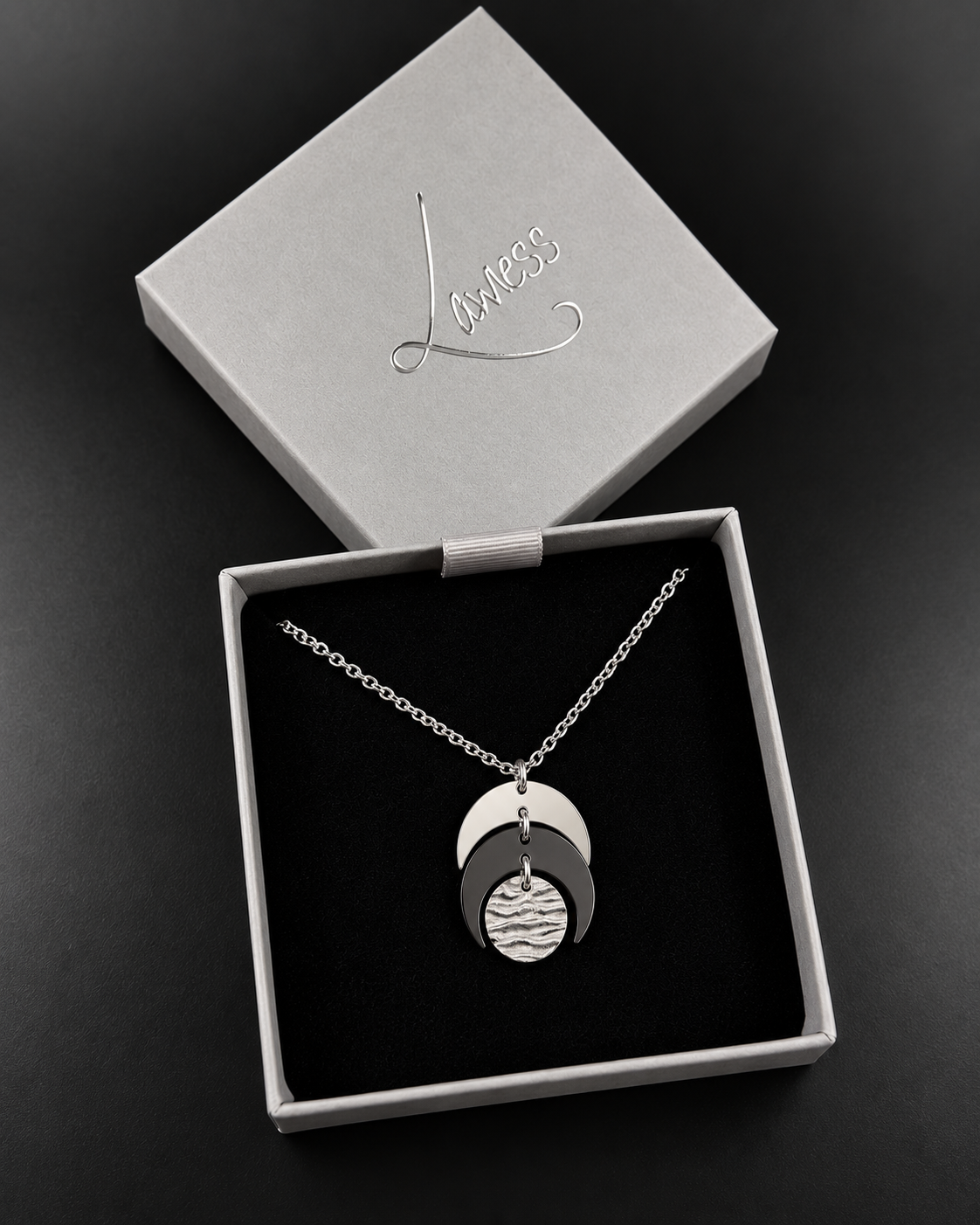 Silver and black Luna Phase Necklace featuring layered crescent shapes and a textured silver lunar disc on a silver chain against a black background.
