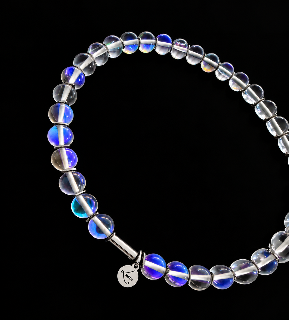 Nebulae Field Necklace featuring a strand of 10mm transparent iridescent glass beads with blue, violet and gold reflections, silver spacers, a stainless steel screw clasp and Lawless logo tag against a black background.