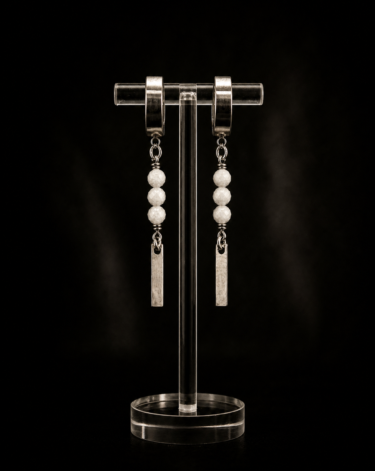Pair of earrings on a clear stand against a black background