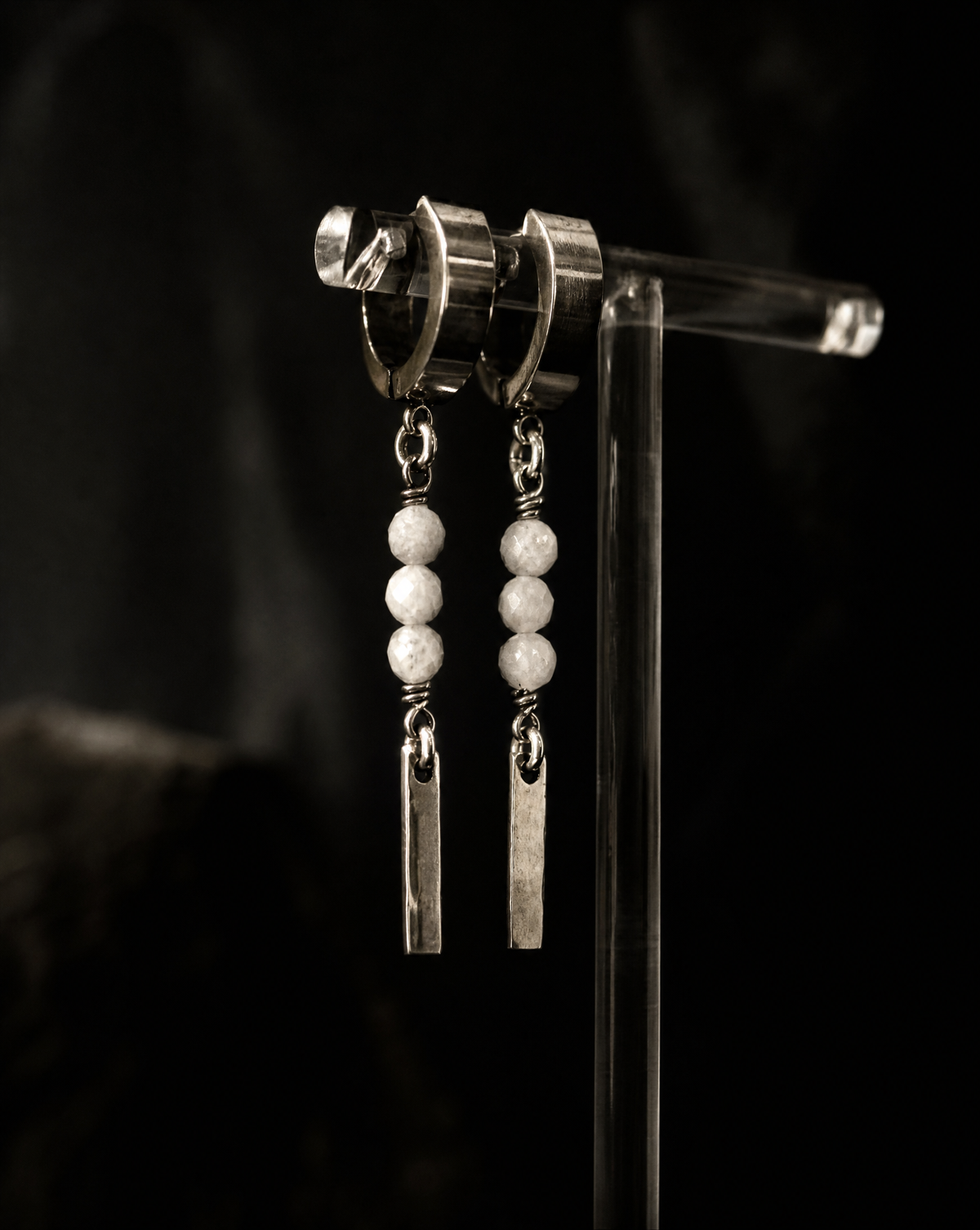 Silver earrings with beads on a clear stand against a dark background