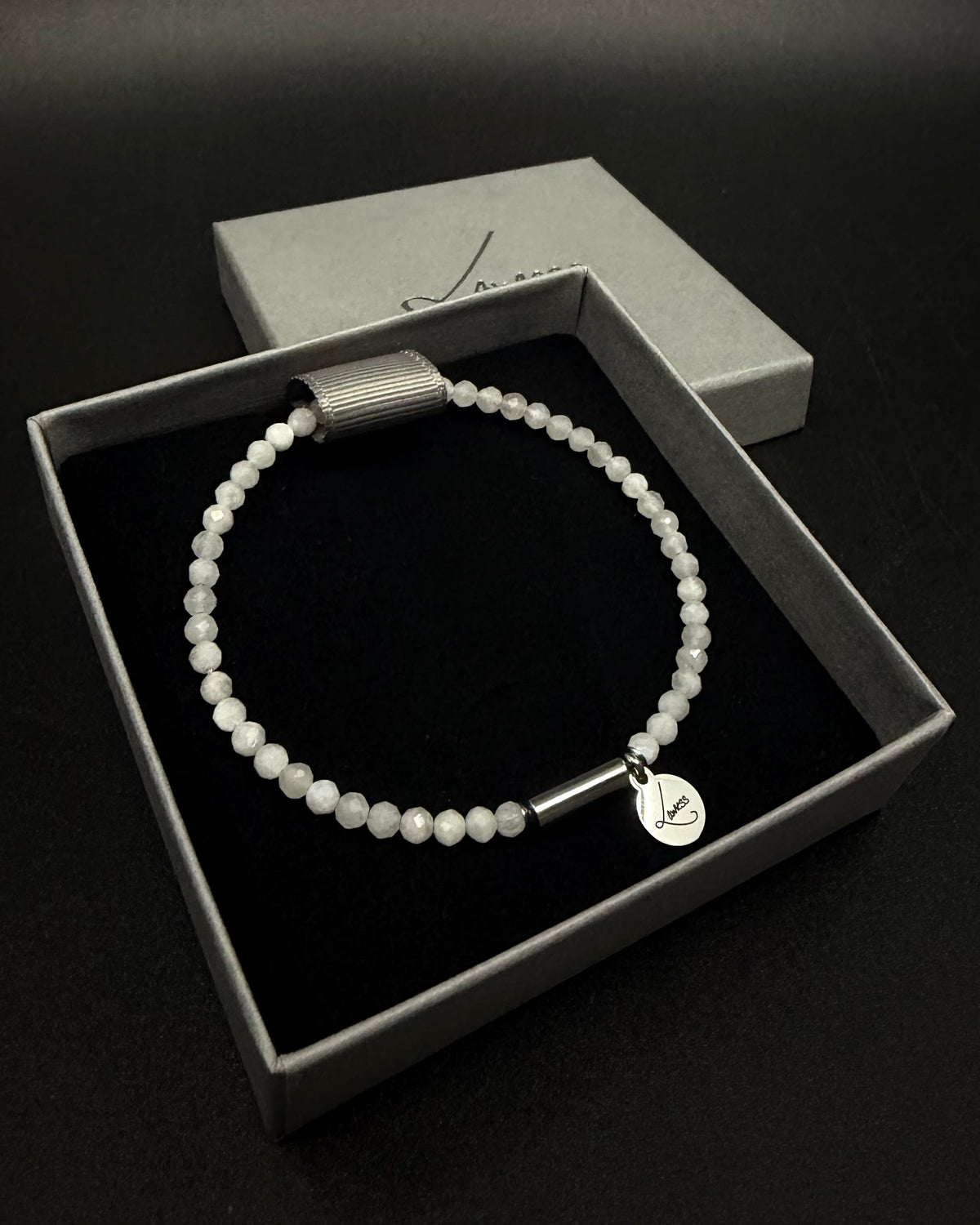 Selene Anew Bracelet made from faceted white moonstone beads with a silver cylindrical screw clasp and round Lawless logo tag against a black background.