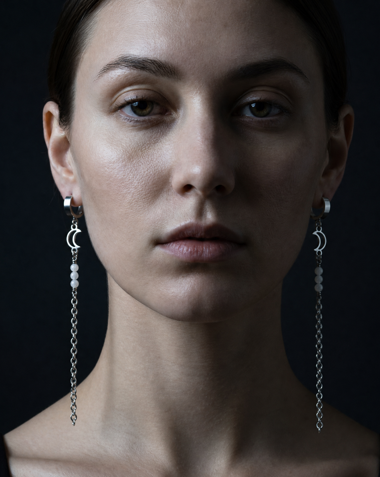Close-up of a woman wearing long, dangling earrings against a dark background