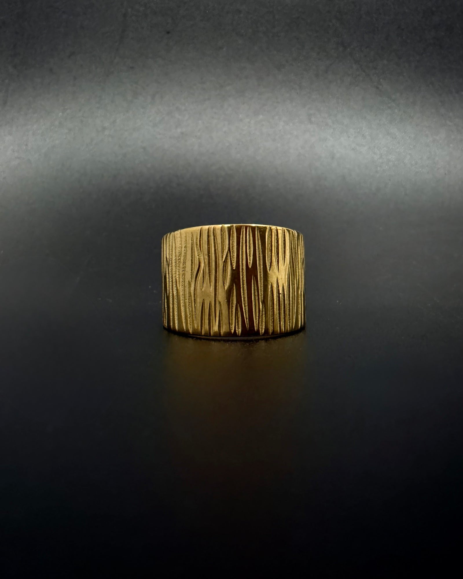 Gold Theia Frequency adjustable ring with a wide tapered band and irregular linear waveform texture against a black background.