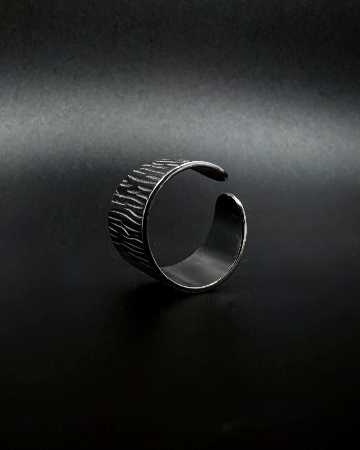 Silver Theia Frequency adjustable ring with a wide tapered band and irregular linear waveform texture against a black background.