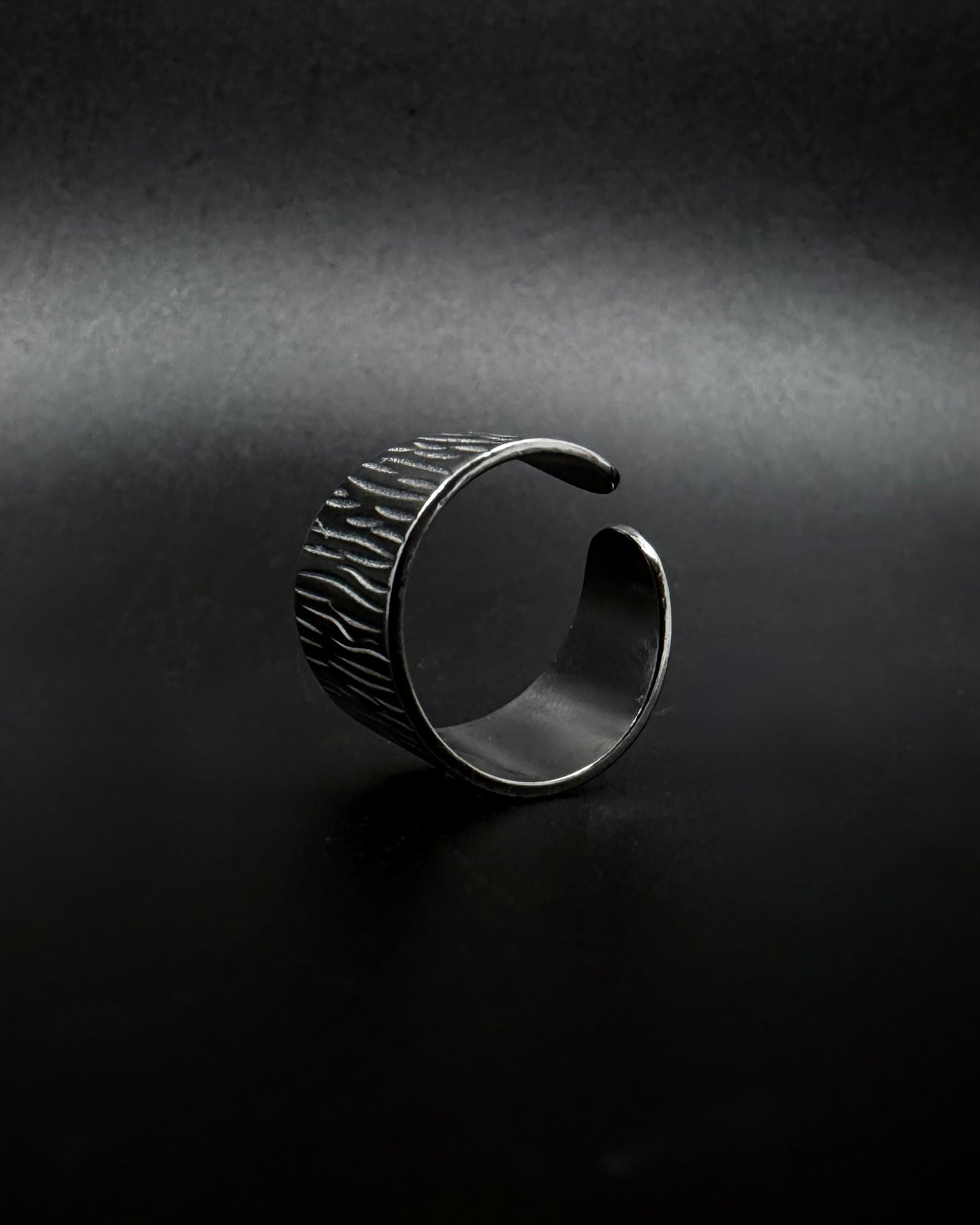 Silver Theia Frequency adjustable ring with a wide tapered band and irregular linear waveform texture against a black background.