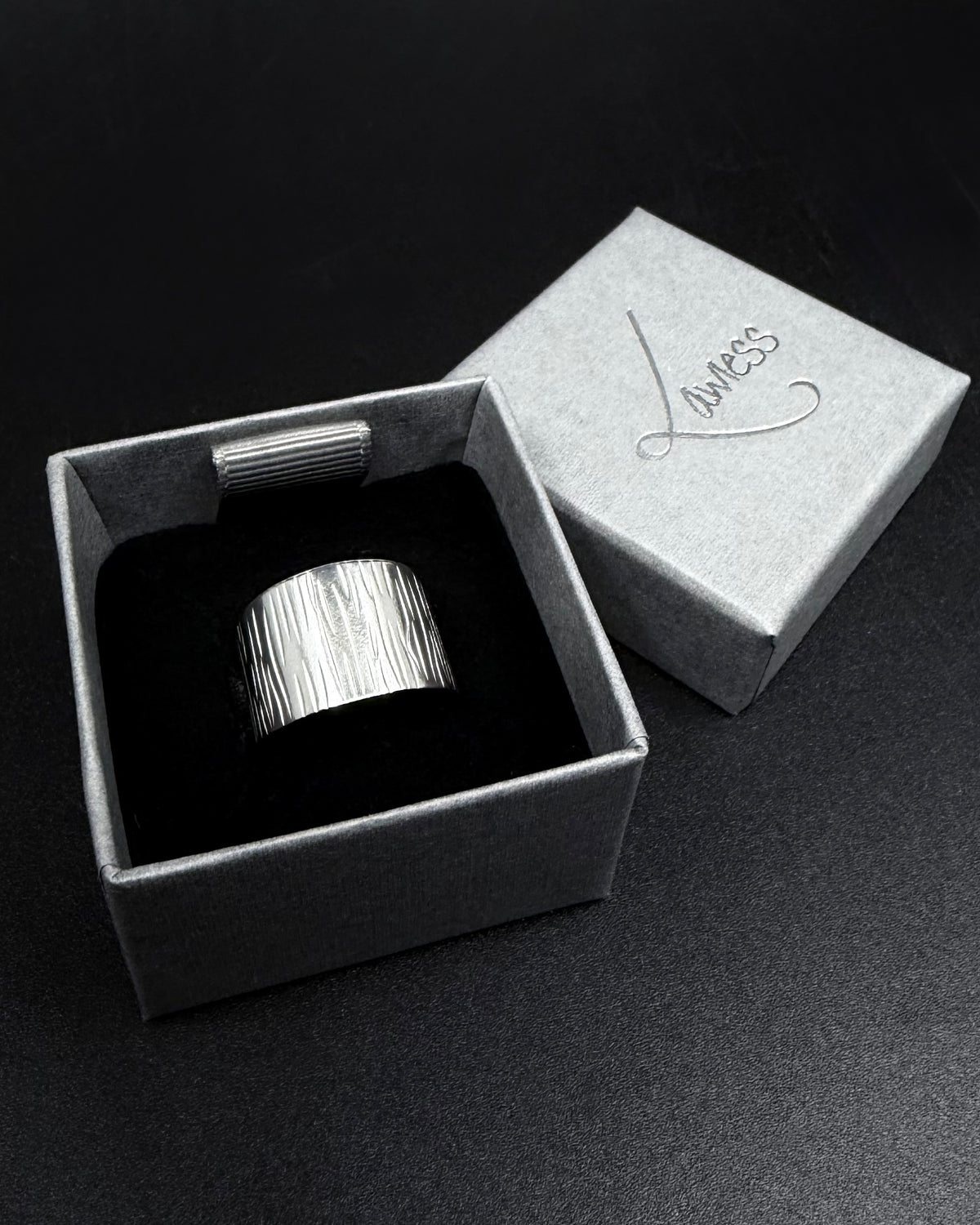 Silver Theia Frequency adjustable ring with a wide tapered band and irregular linear waveform texture against a black background.