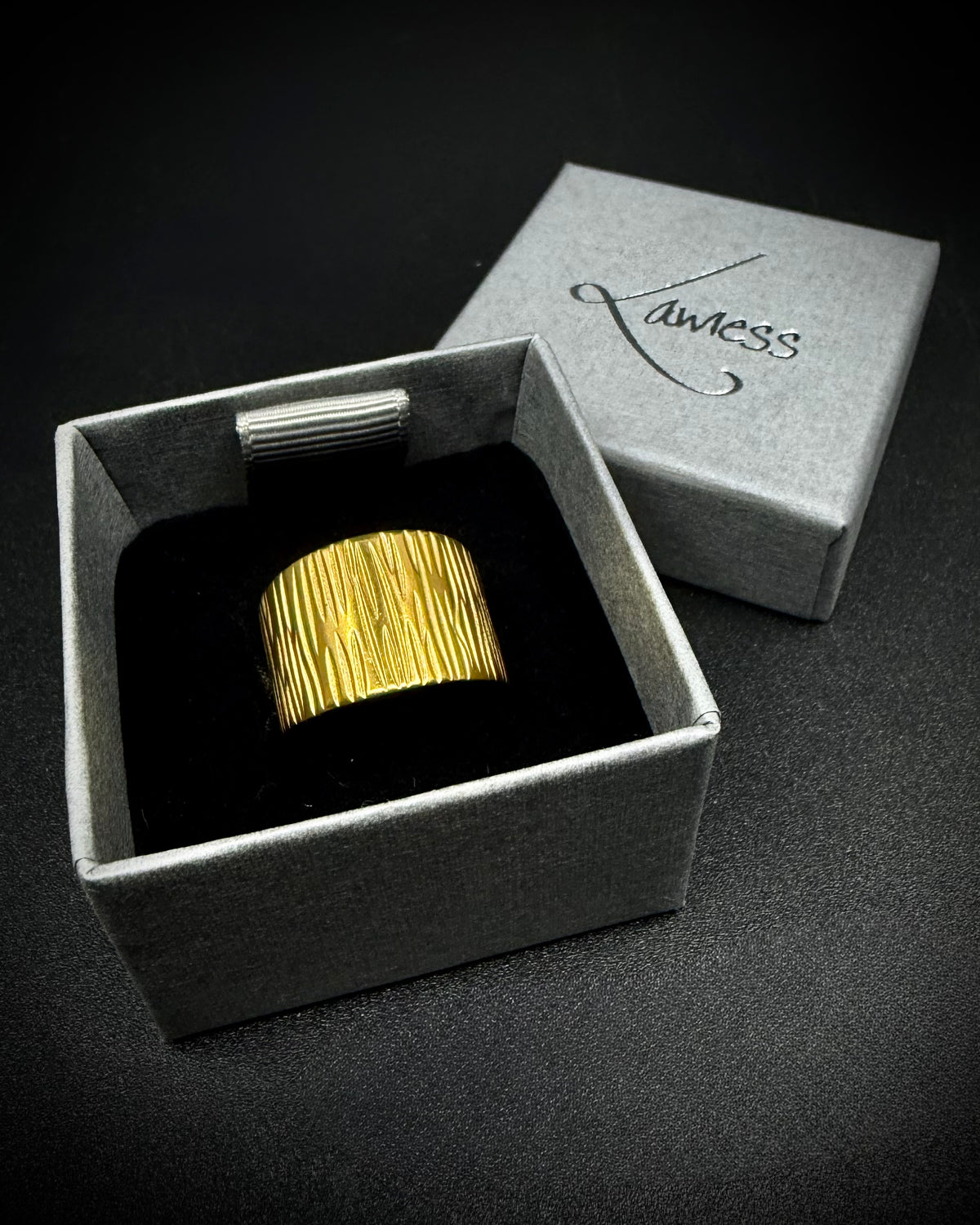 Gold Theia Frequency adjustable ring with a wide tapered band and irregular linear waveform texture against a black background.