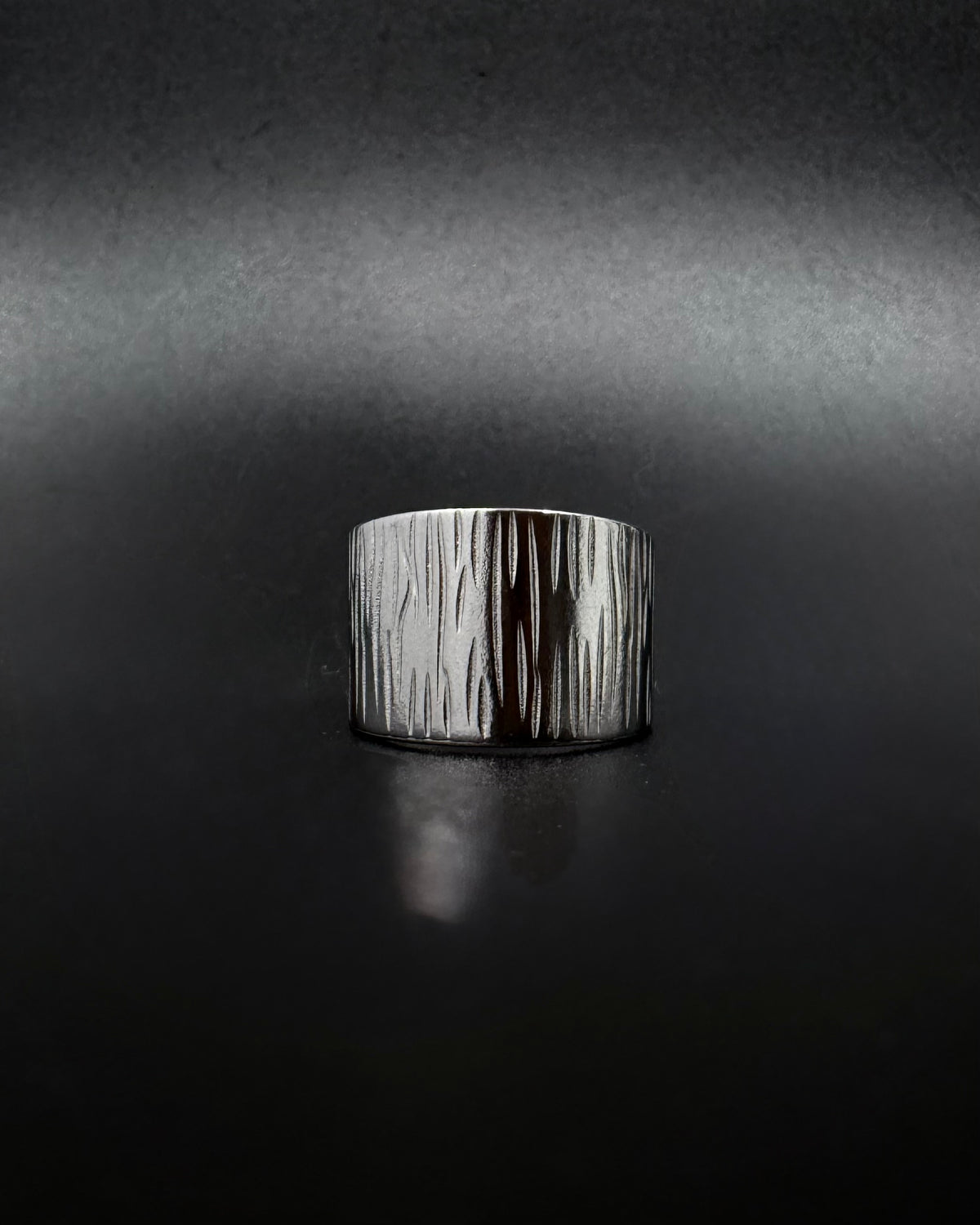 Silver Theia Frequency adjustable ring with a wide tapered band and irregular linear waveform texture against a black background.