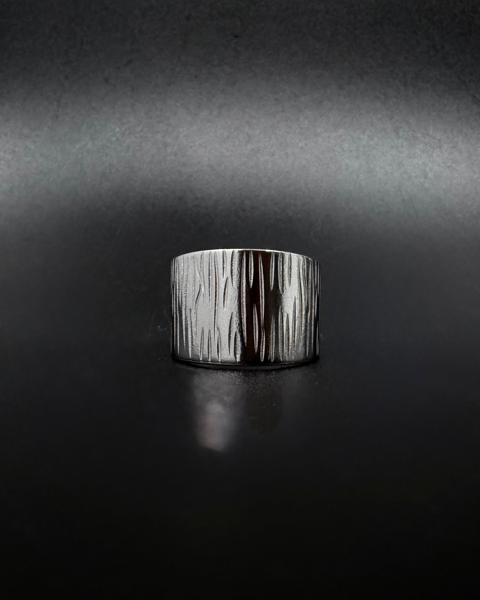 Silver Theia Frequency adjustable ring with a wide tapered band and irregular linear waveform texture against a black background.