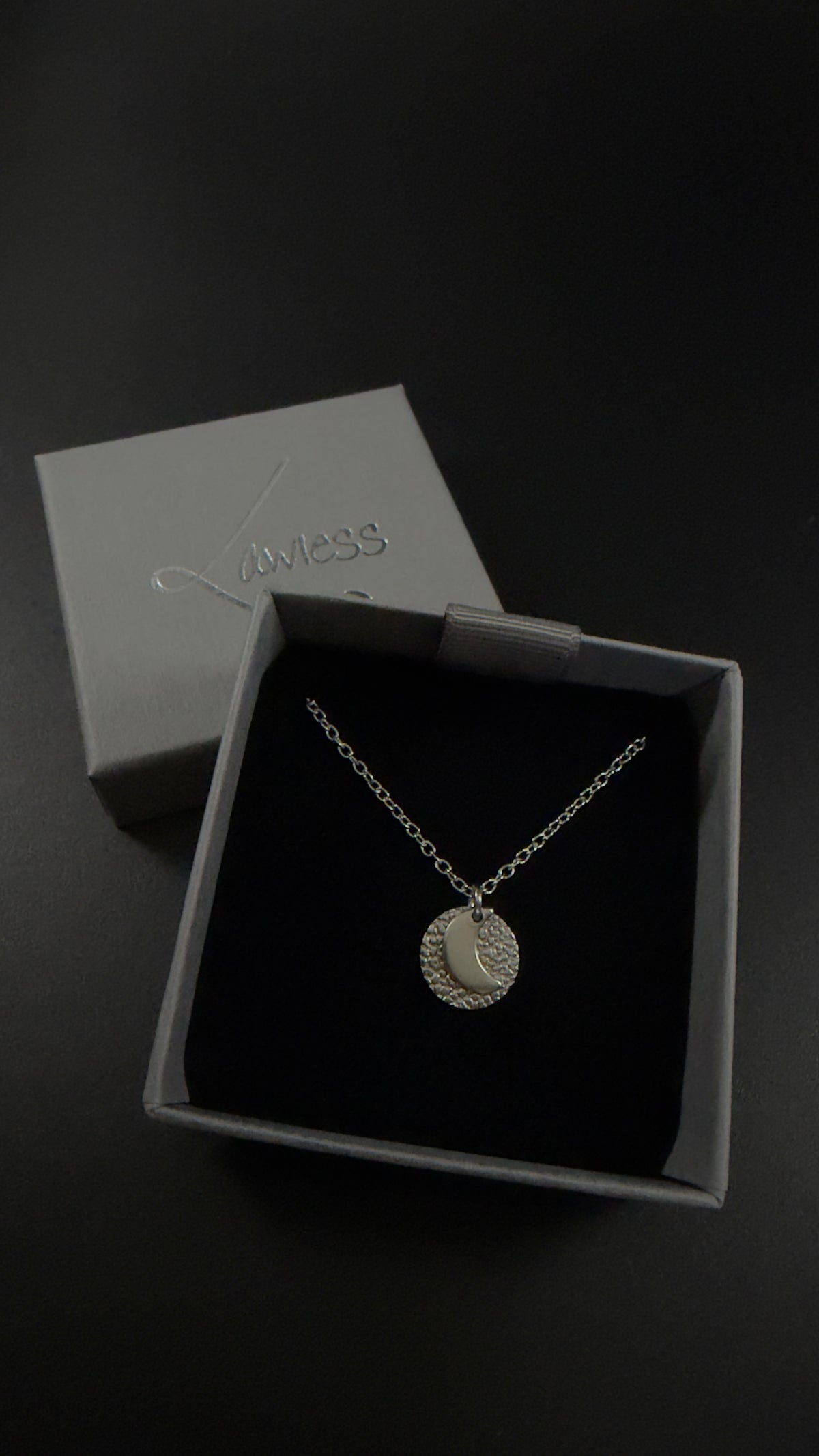 Urania Cipher necklaces in silver stainless steel, showing the polished crescent moon and star faces against textured silver discs on silver chains. 