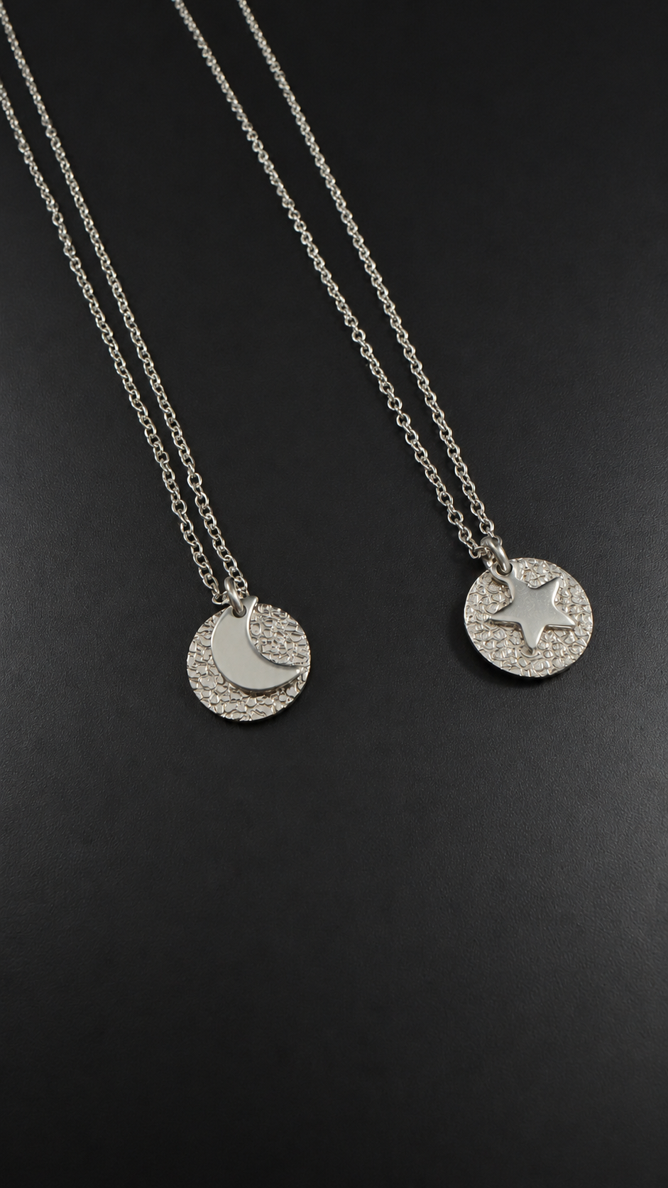 Urania Cipher necklaces in silver stainless steel, showing the polished crescent moon and star faces against textured silver discs on silver chains.