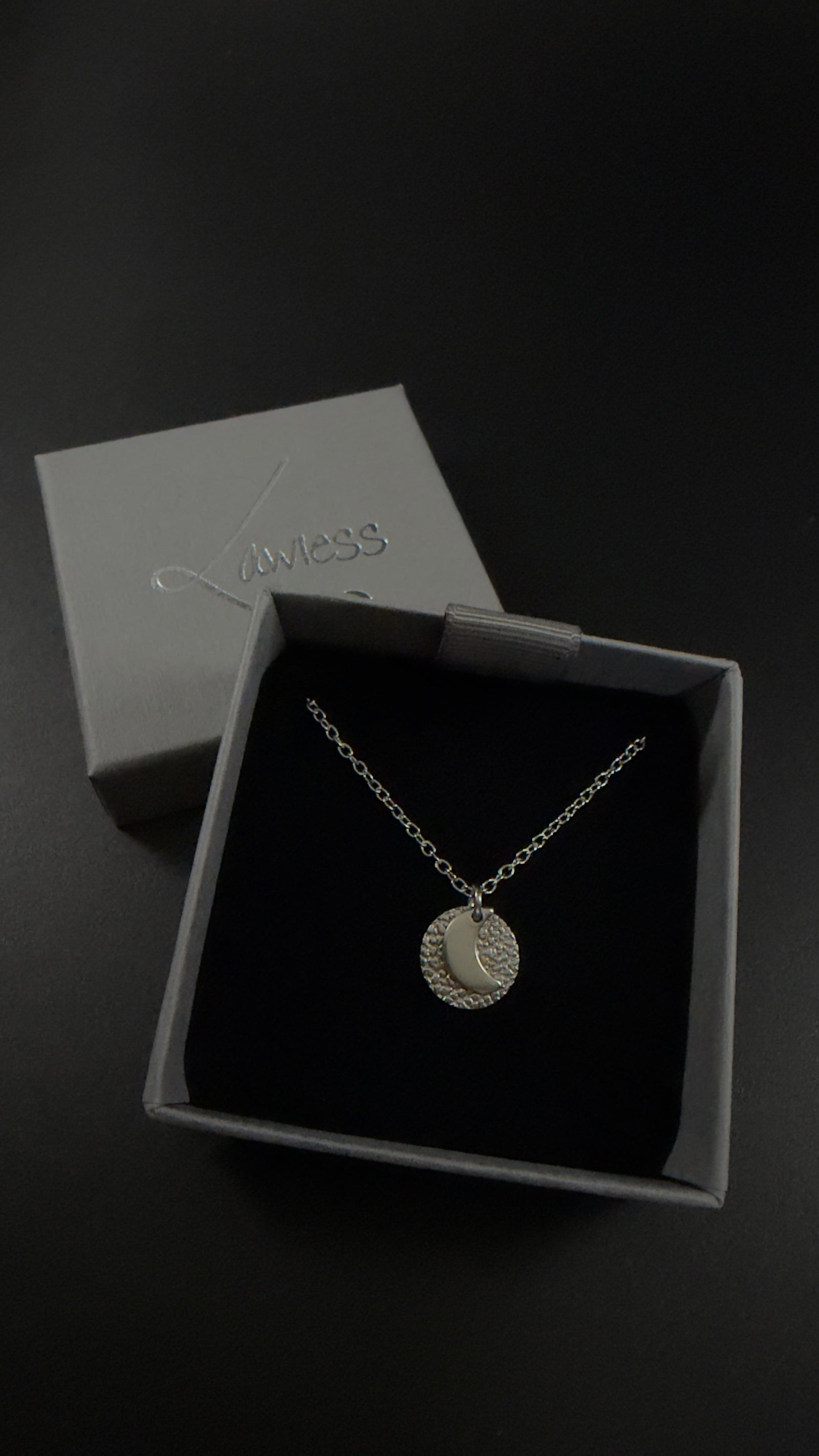 Urania Cipher necklaces in silver stainless steel, showing the polished crescent moon and star faces against textured silver discs on silver chains.