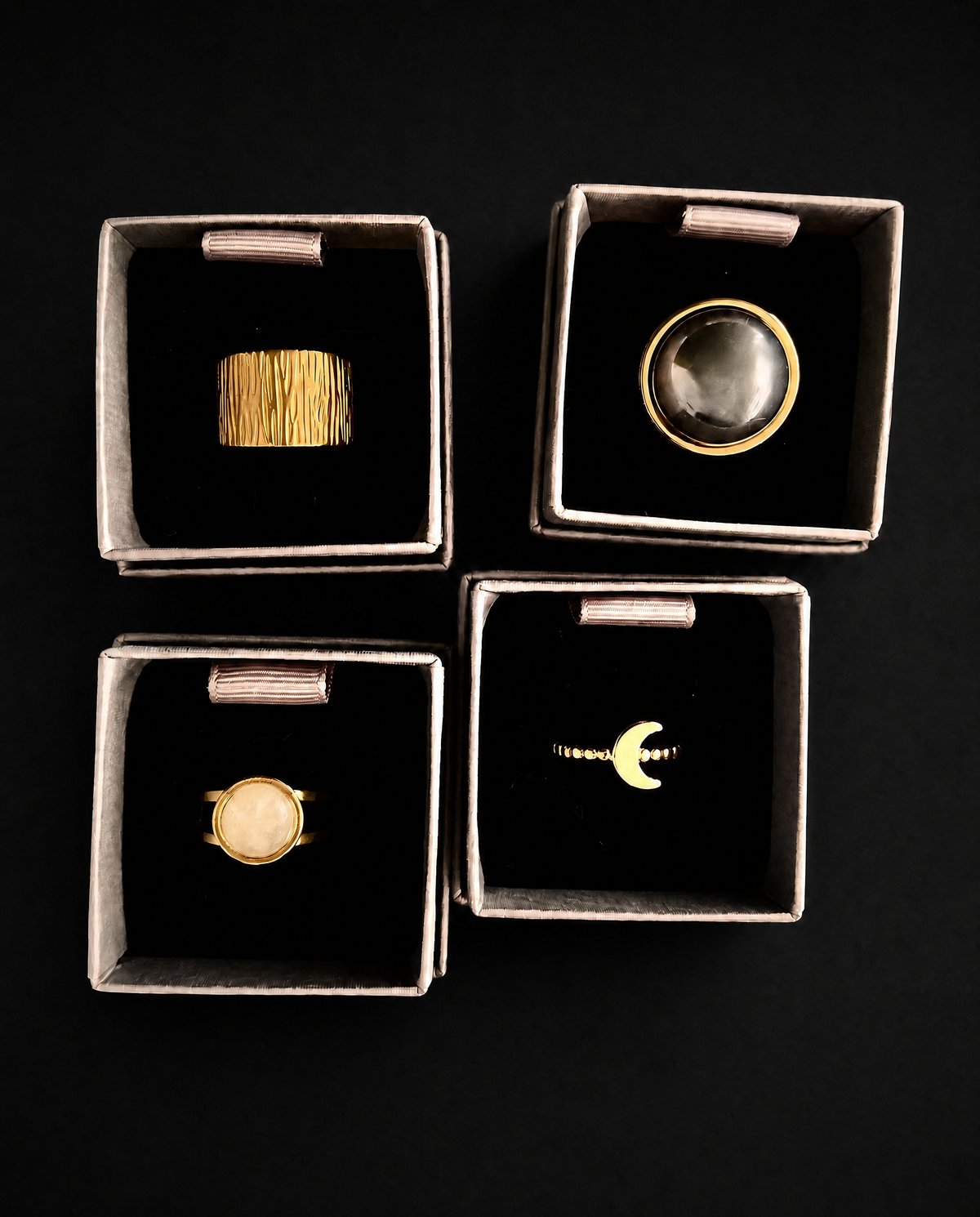 Overhead view of four individually boxed gold rings from the Nebulae × Cassini set, including dome, graduated, celestial moon and quartz designs.