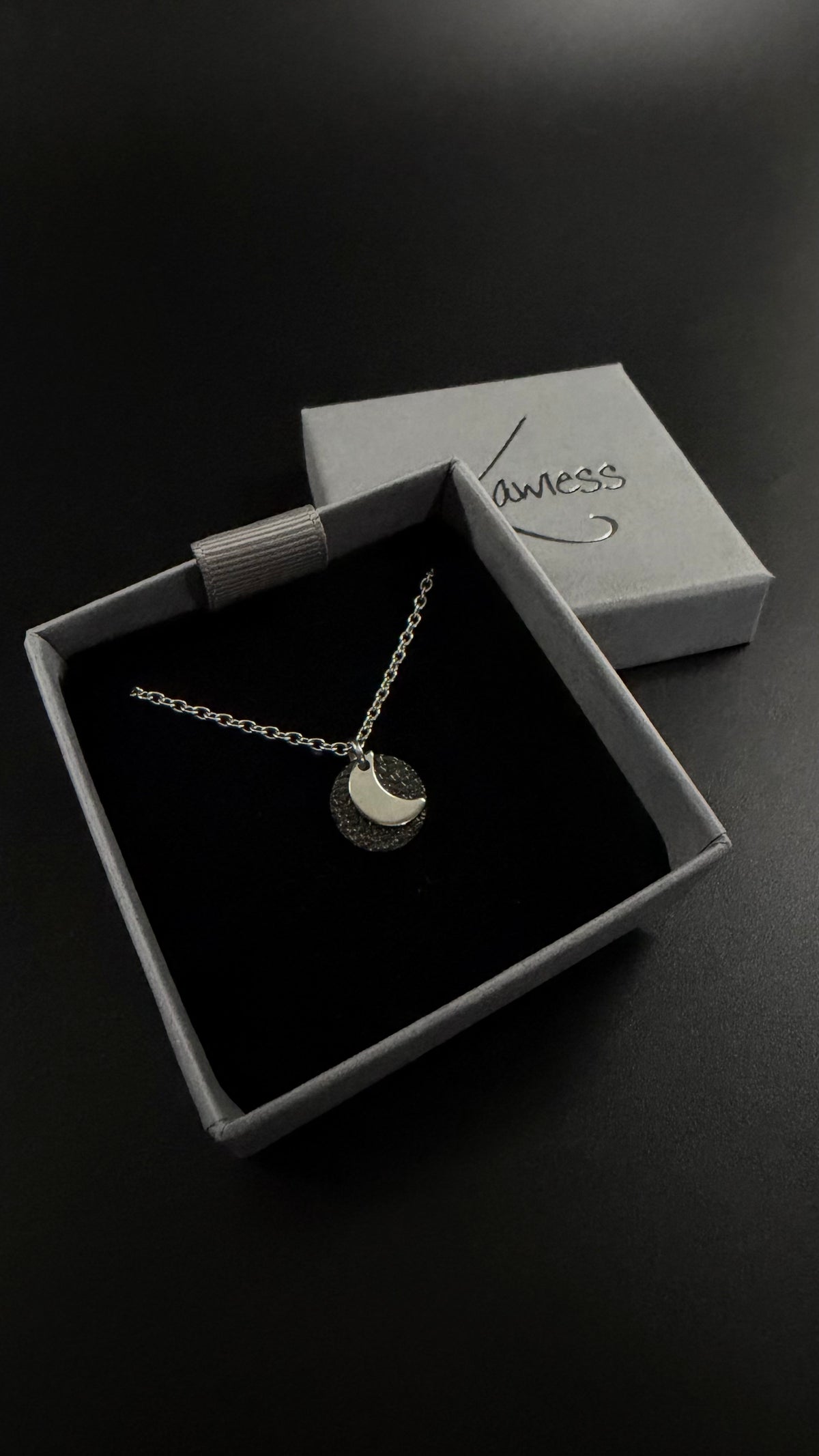 Urania Cipher Necklace with a silver chain and textured black reversible pendant featuring a silver crescent moon on one side and a star on the other.