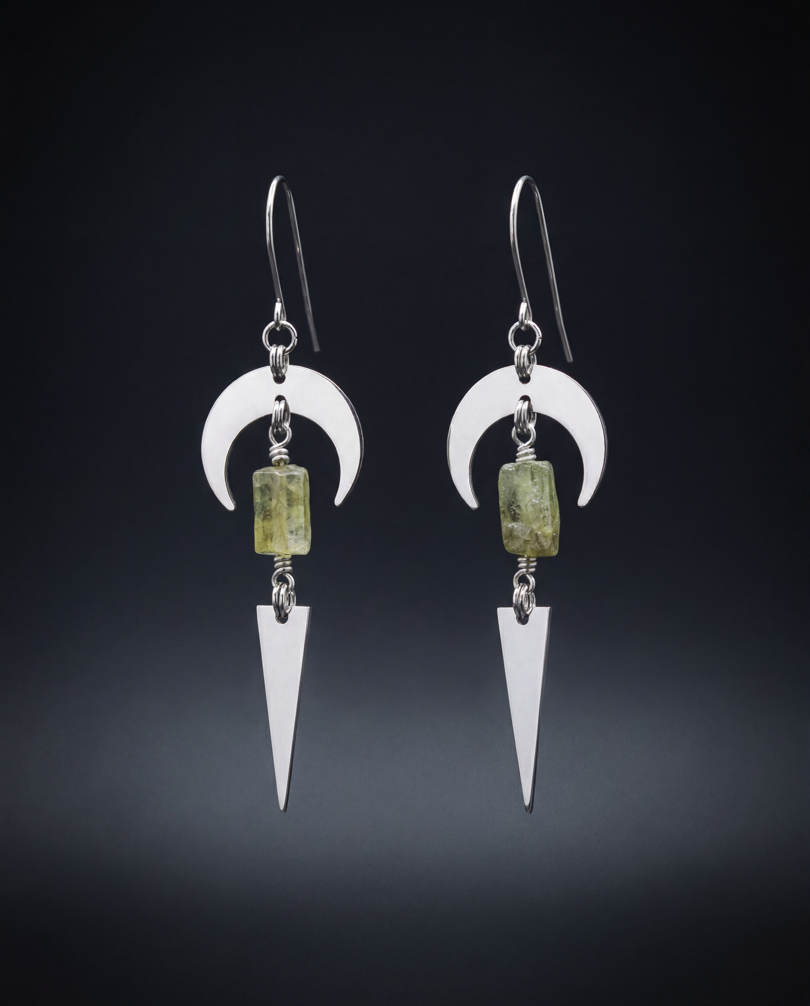 Pair of silver Orion Arc drop earrings featuring crescent-shaped steel arcs, rectangular green peridot gemstones and long pointed pendants.