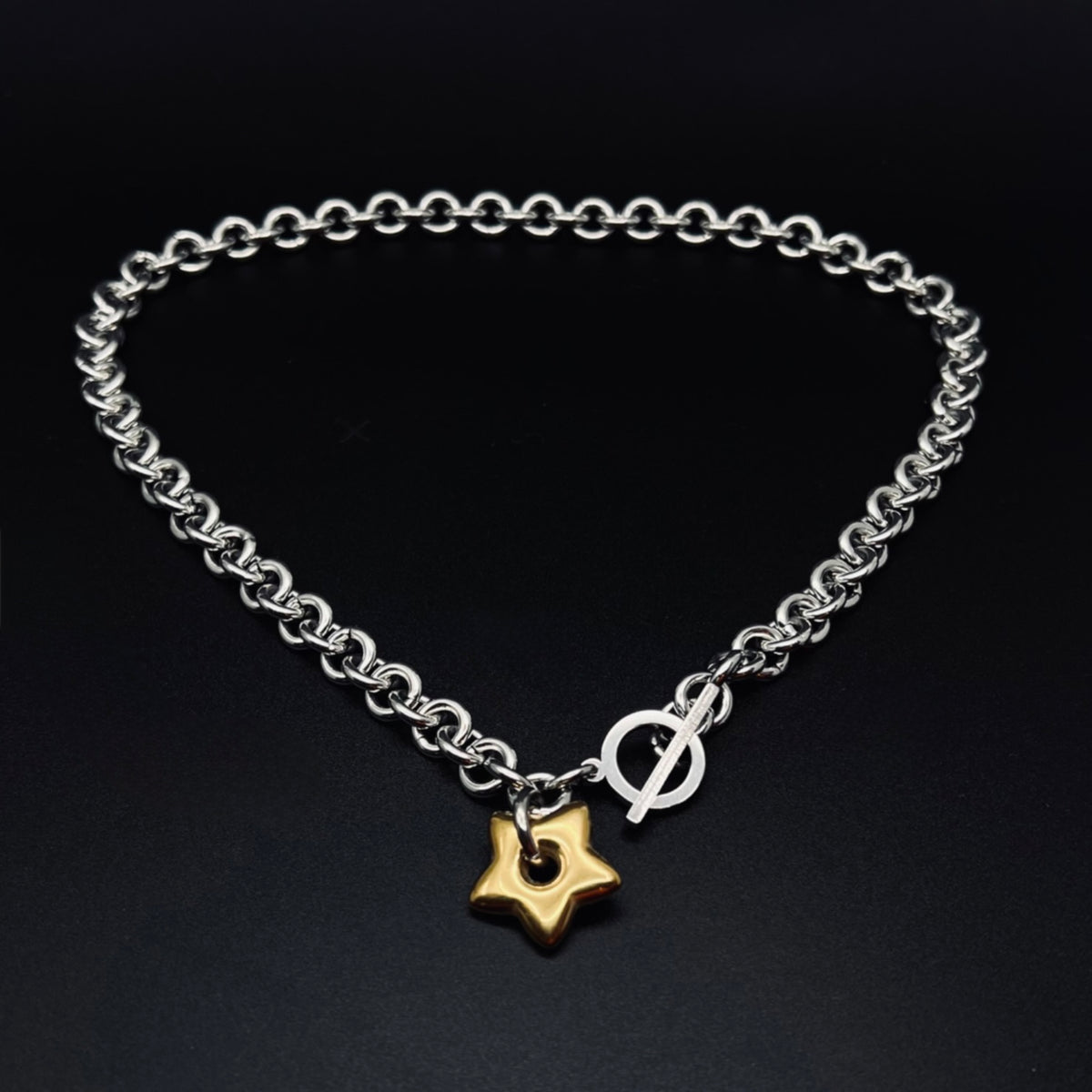 Silver stainless steel chain necklace with gold star pendant and toggle clasp, Urania Axis Necklace by Lawless Jewellery on black background.
