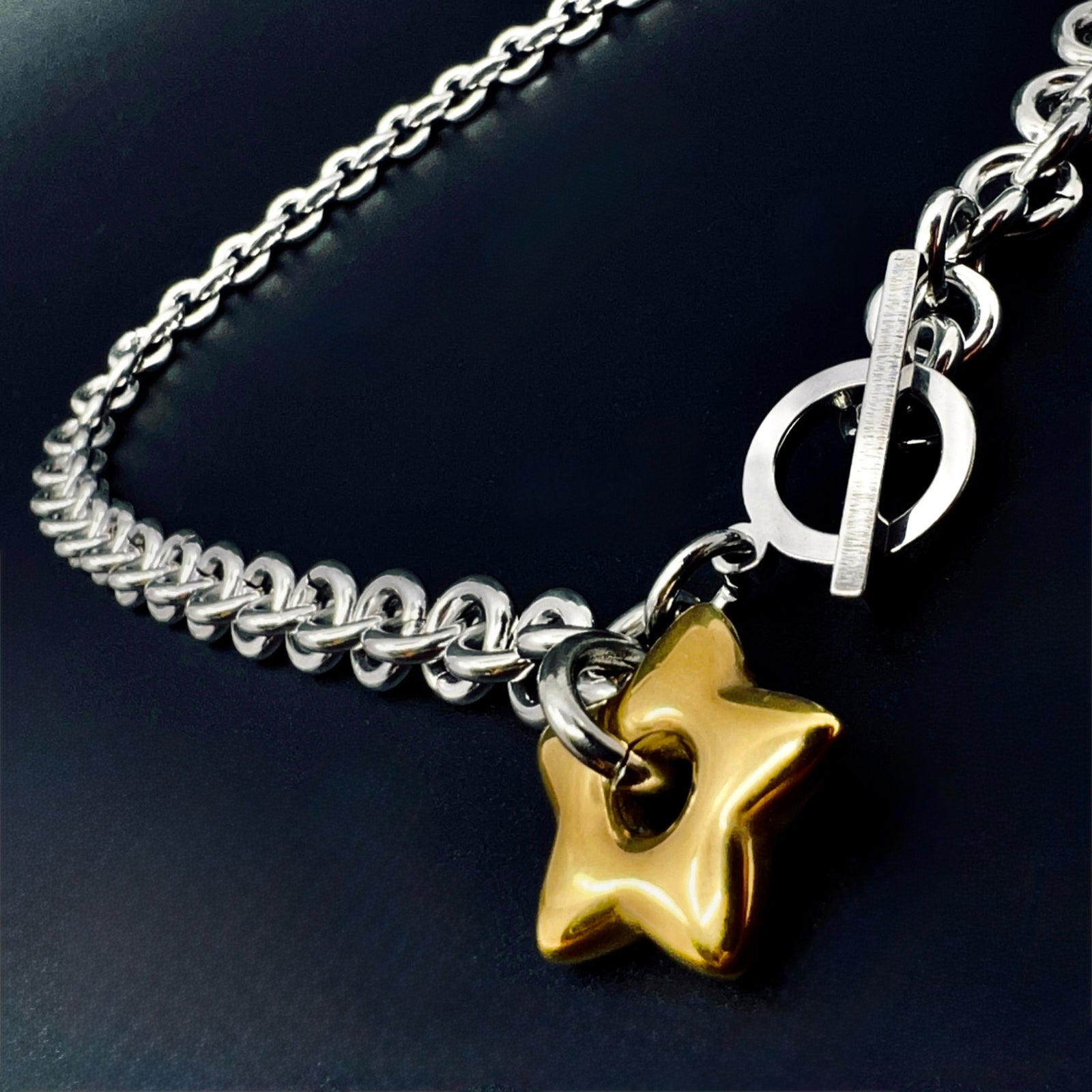 Silver stainless steel chain necklace with gold star pendant and toggle clasp, Urania Axis Necklace by Lawless Jewellery on black background.