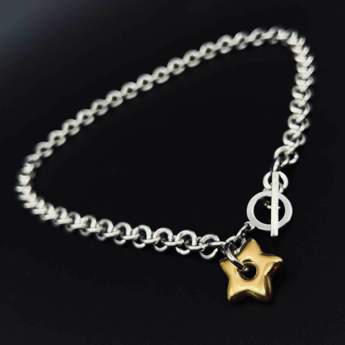 Silver stainless steel chain necklace with gold star pendant and toggle clasp, Urania Axis Necklace by Lawless Jewellery on black background.
