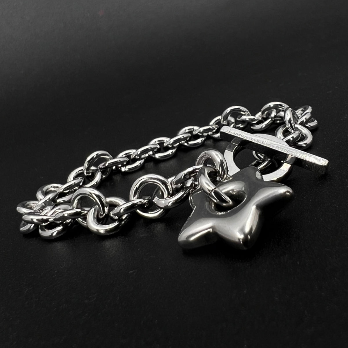 All-silver stainless steel bracelet featuring an 18mm star charm on a polished chain with toggle clasp, photographed on a dark background.