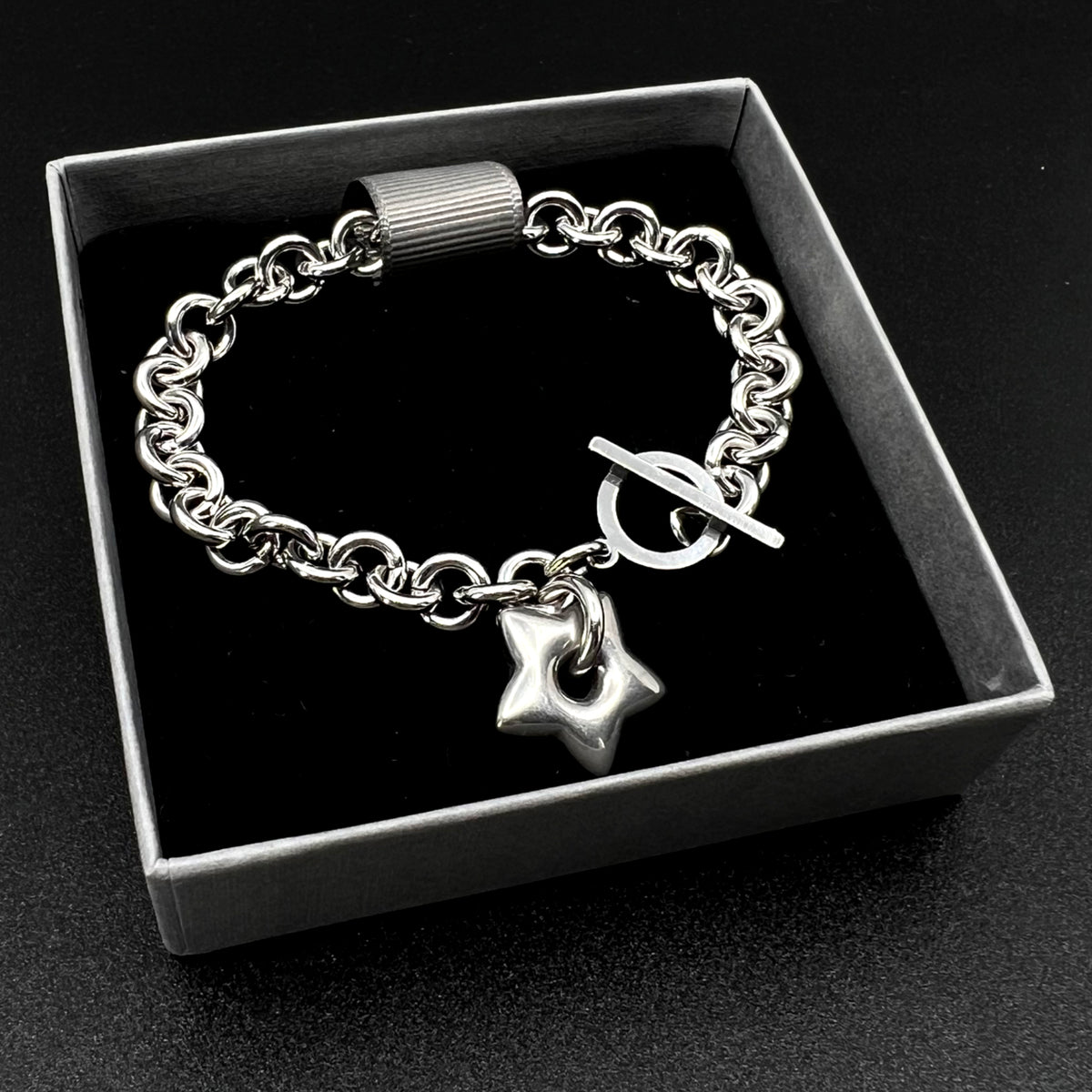 All-silver stainless steel bracelet featuring an 18mm star charm on a polished chain with toggle clasp, photographed on a dark background.
