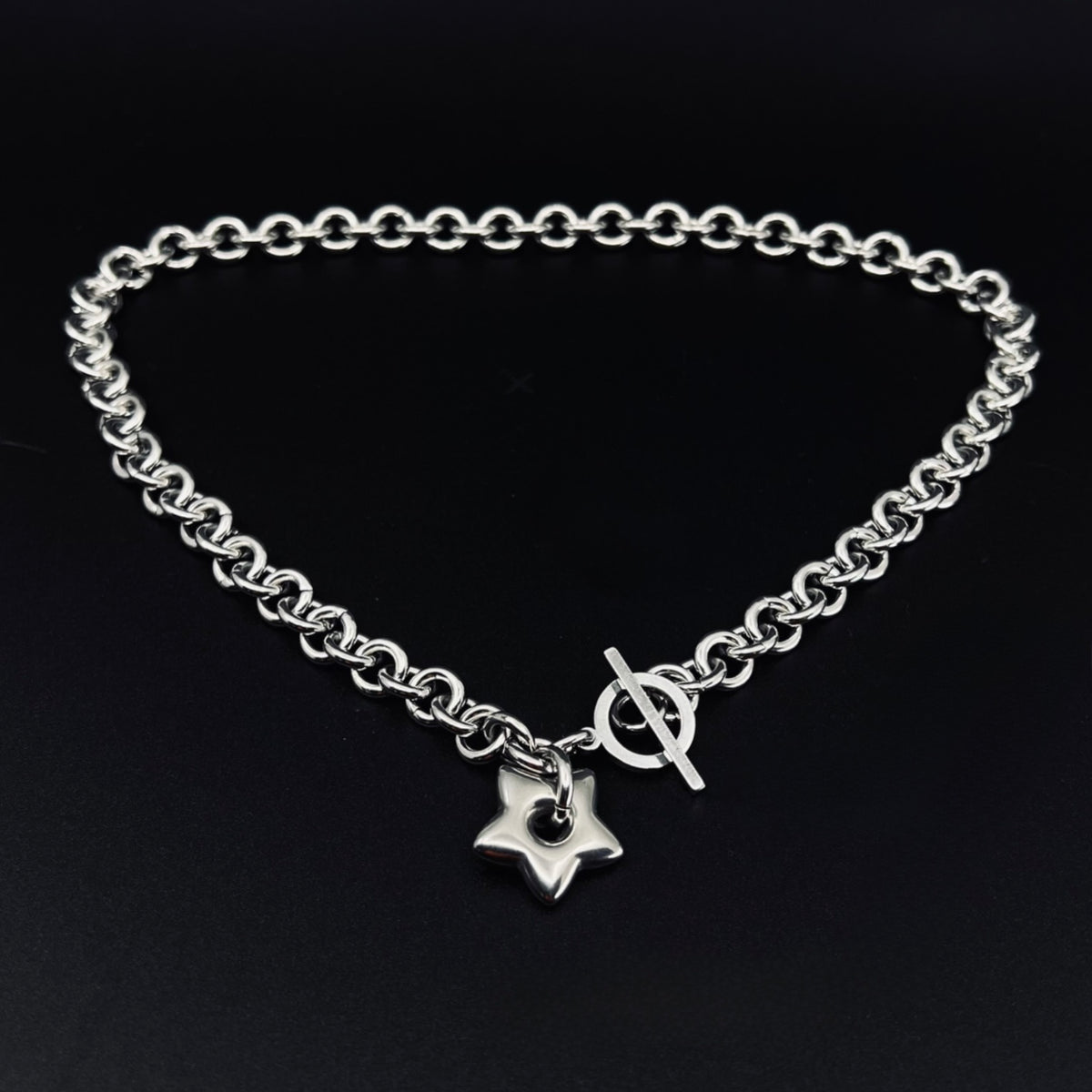 Silver stainless steel chain necklace with gold star pendant and toggle clasp, Urania Axis Necklace by Lawless Jewellery on black background
