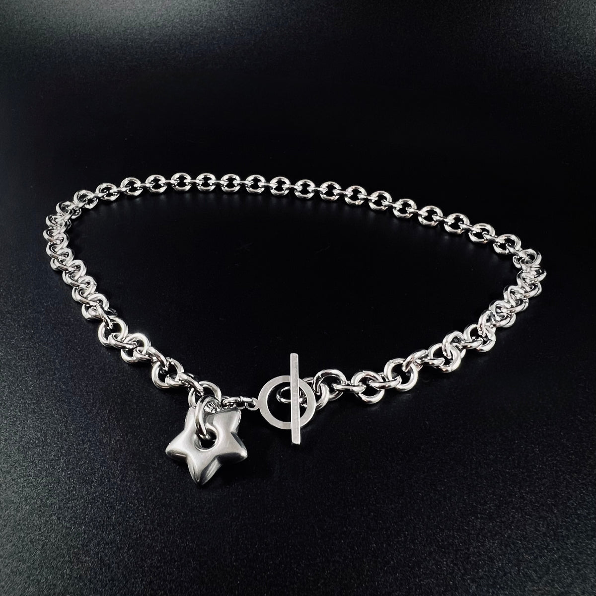 Silver stainless steel chain necklace with gold star pendant and toggle clasp, Urania Axis Necklace by Lawless Jewellery on black background