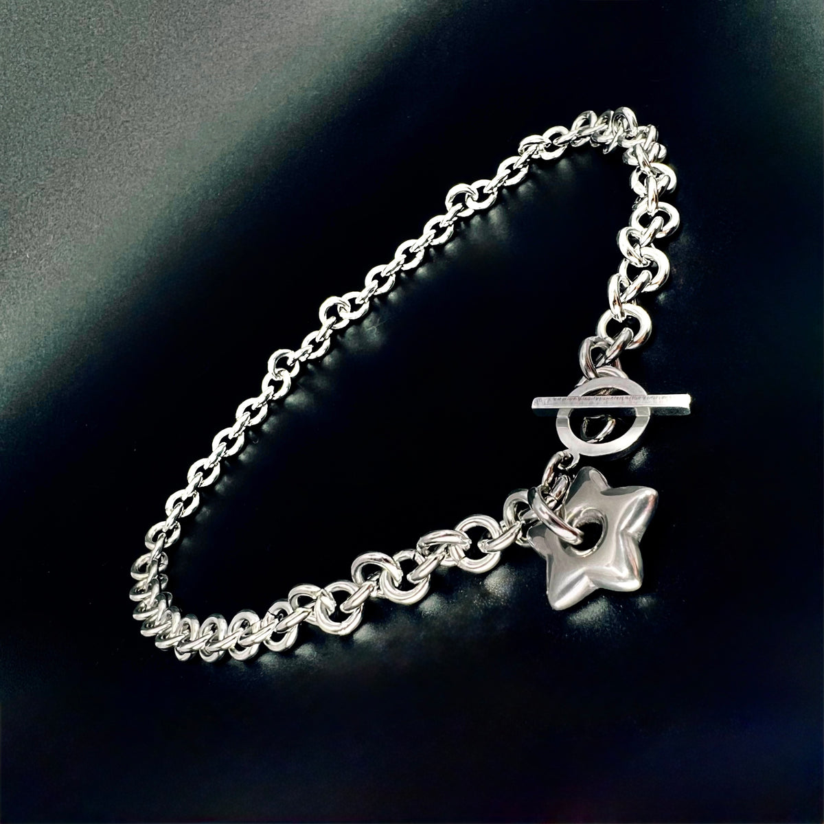 Silver stainless steel chain necklace with gold star pendant and toggle clasp, Urania Axis Necklace by Lawless Jewellery on black background