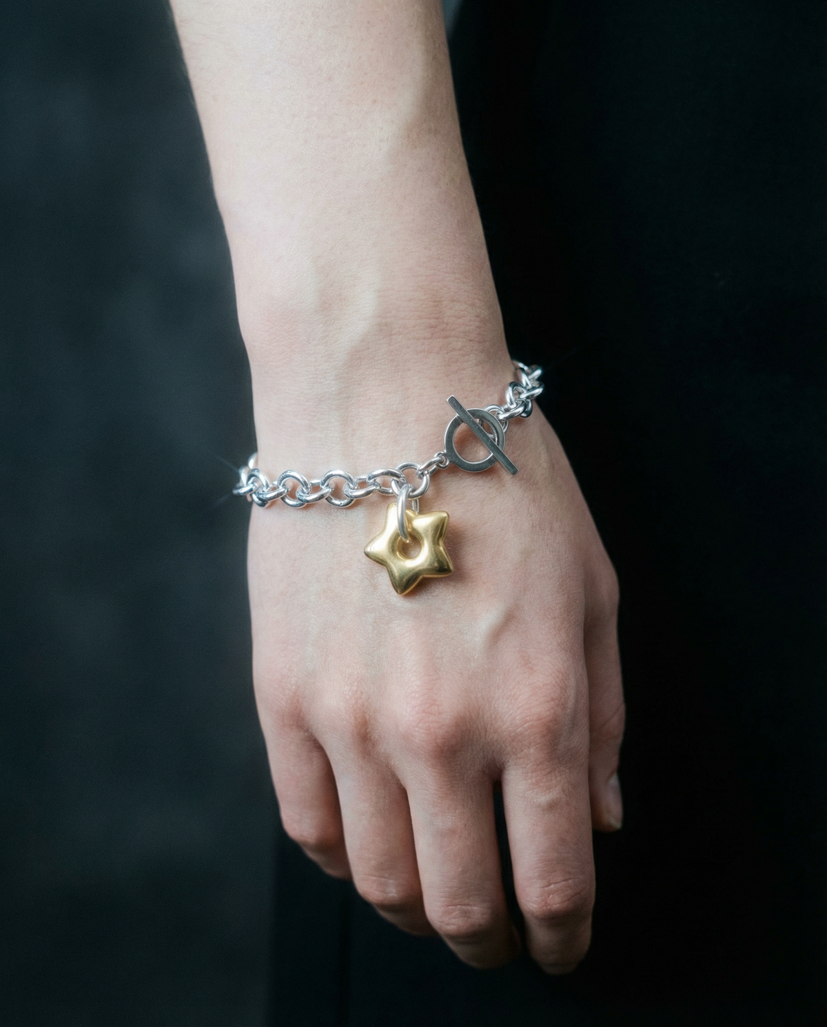 Mixed-metal stainless steel Unisex bracelet featuring an 18mm gold star charm on a silver chain with toggle clasp, photographed on a dark background.